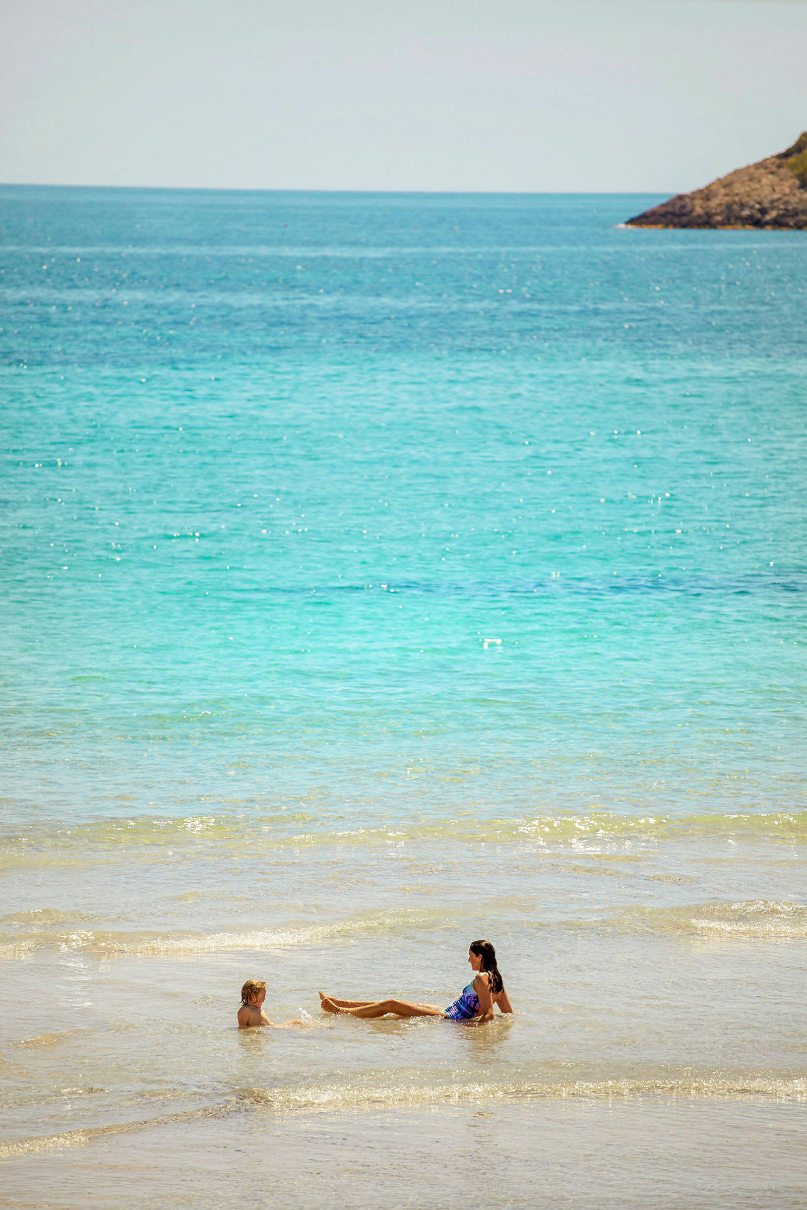 To personer bader i lavt klart vand ved en strand. (AI-genereret tekst)