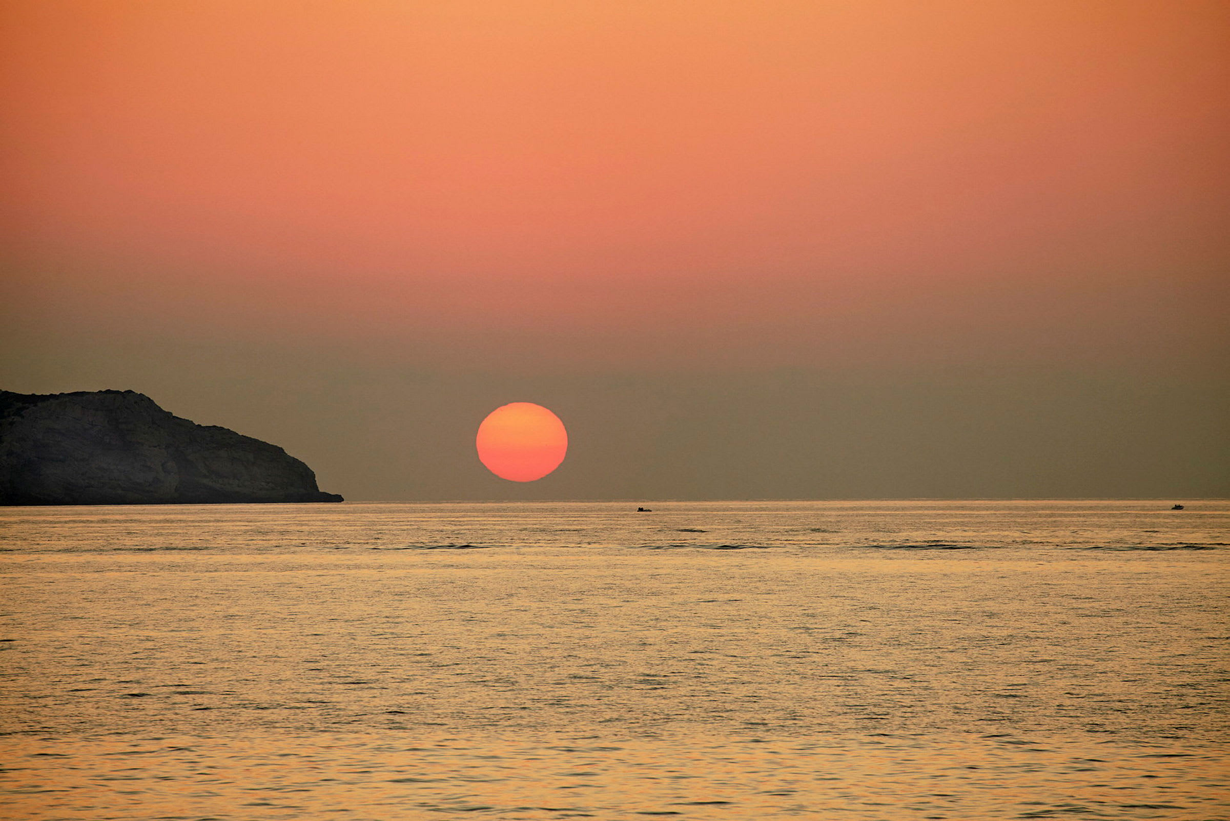 Billede af en solnedgang over havet med en klippeformation til venstre. (AI-genereret tekst)