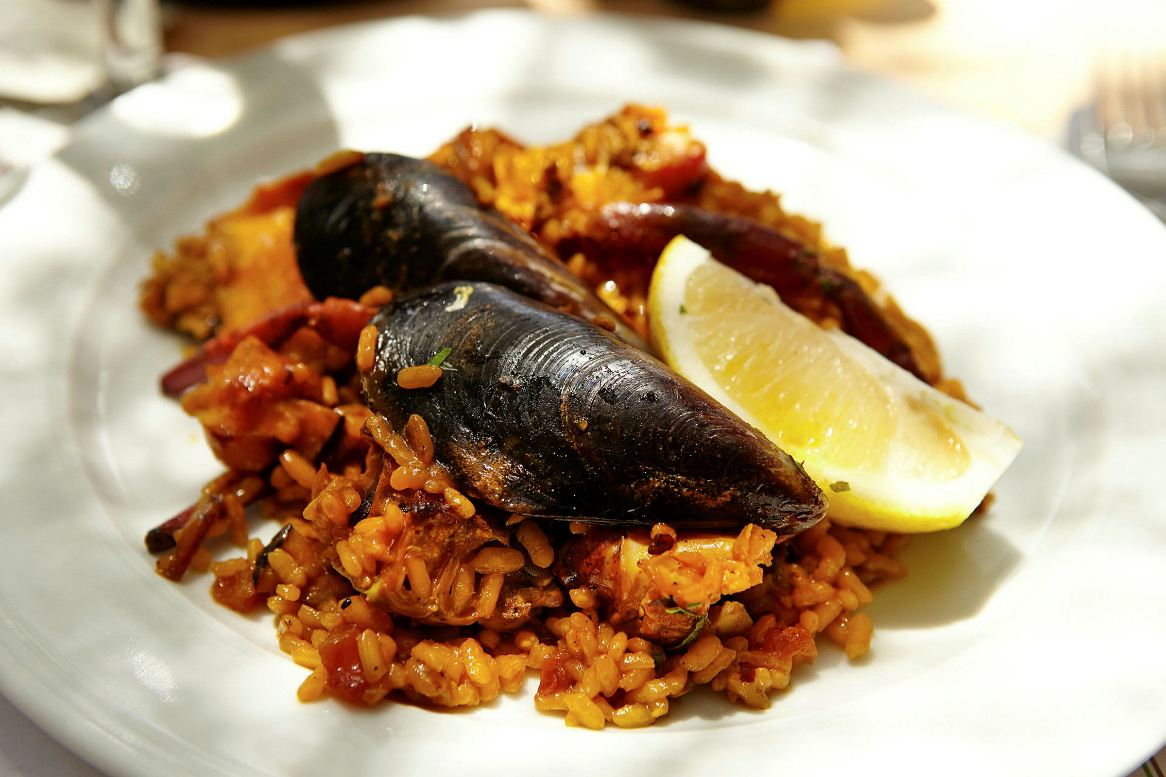 En tallerken med paella bestående af muslinger, krydret ris og en citronskive. (AI-genereret tekst)