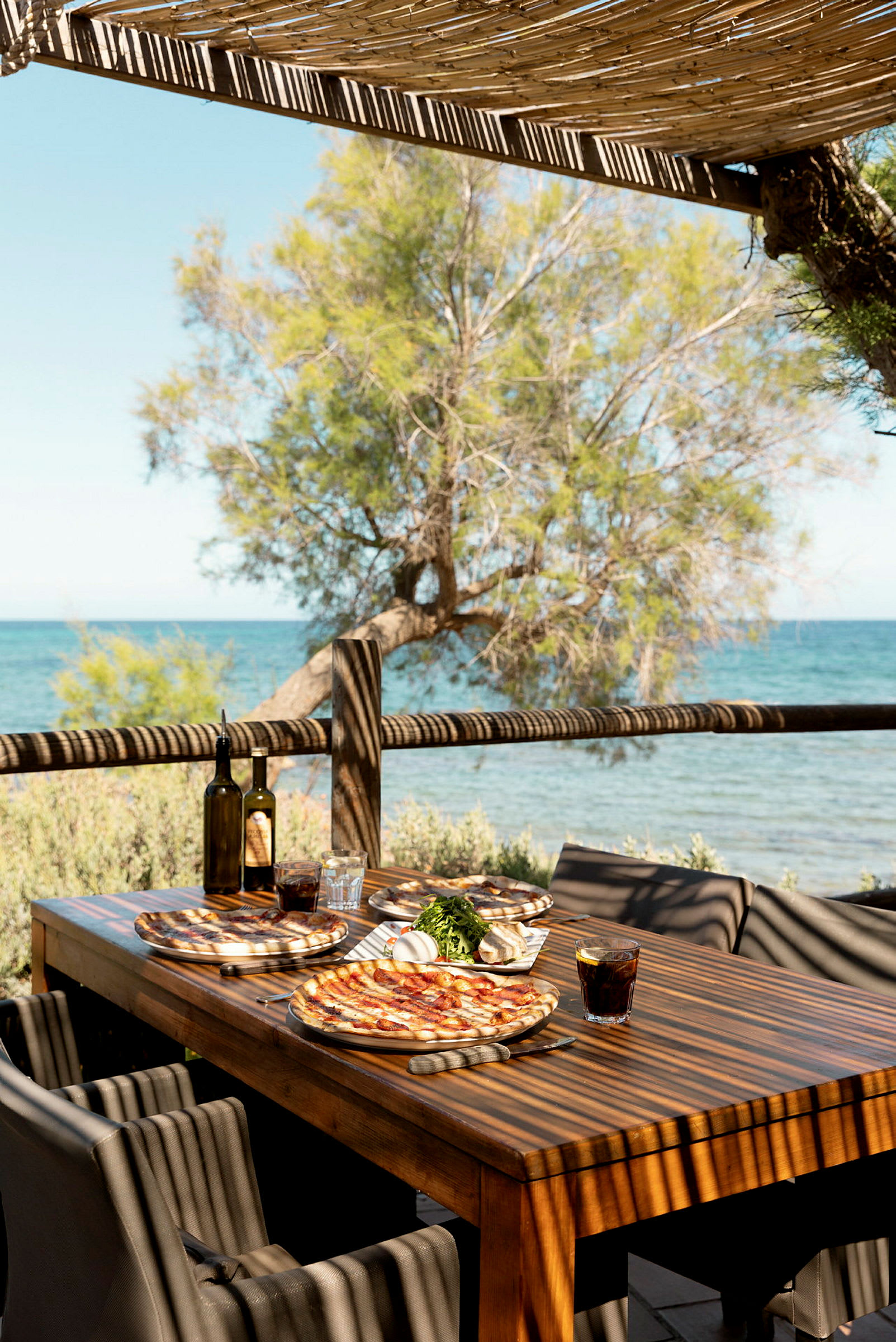 Et bord med pizzaer og drikke under en pergola ved havet. (AI-genereret tekst)