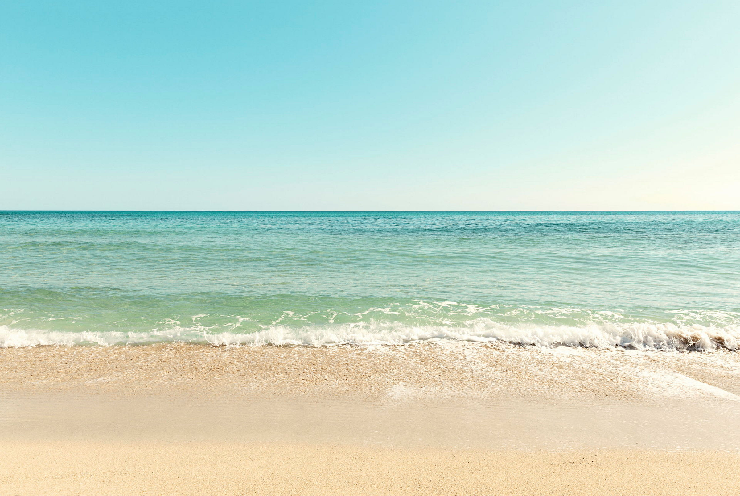 En strand med sand og havet som møder himlen. (AI-genereret tekst)
