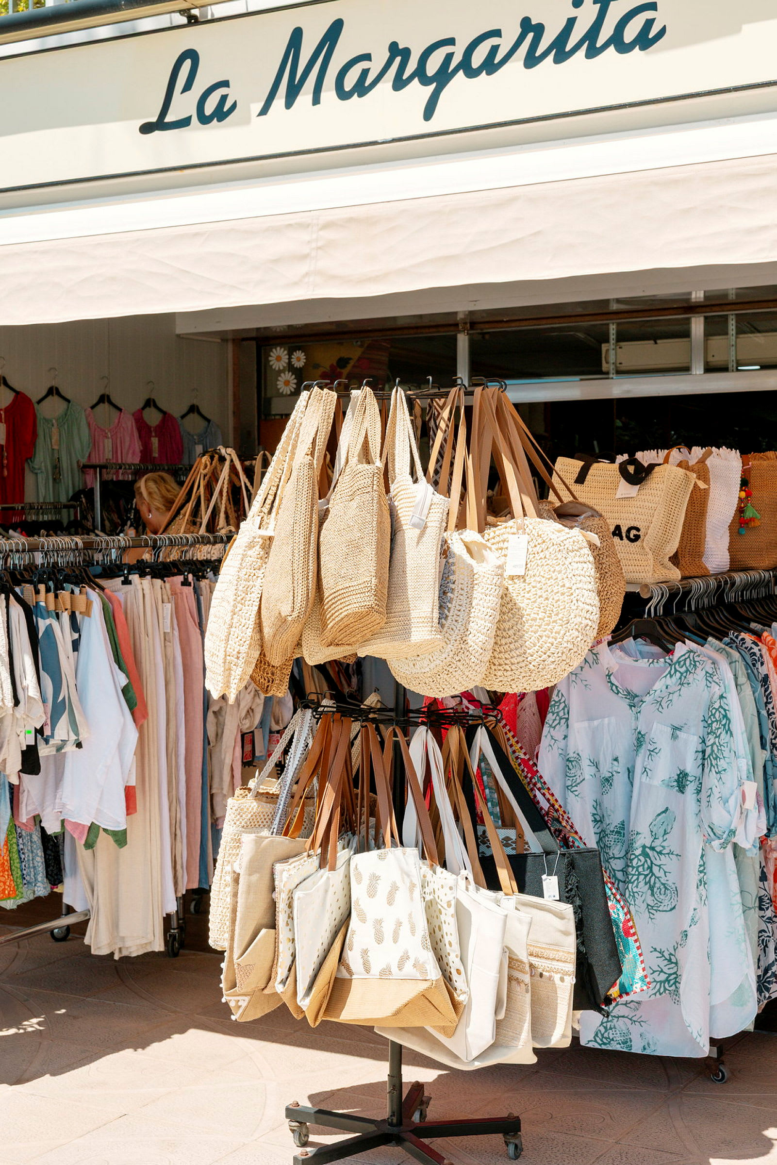 En stativ med strandtasker foran en butik, der sælger tøj og tilbehør. (AI-genereret tekst)