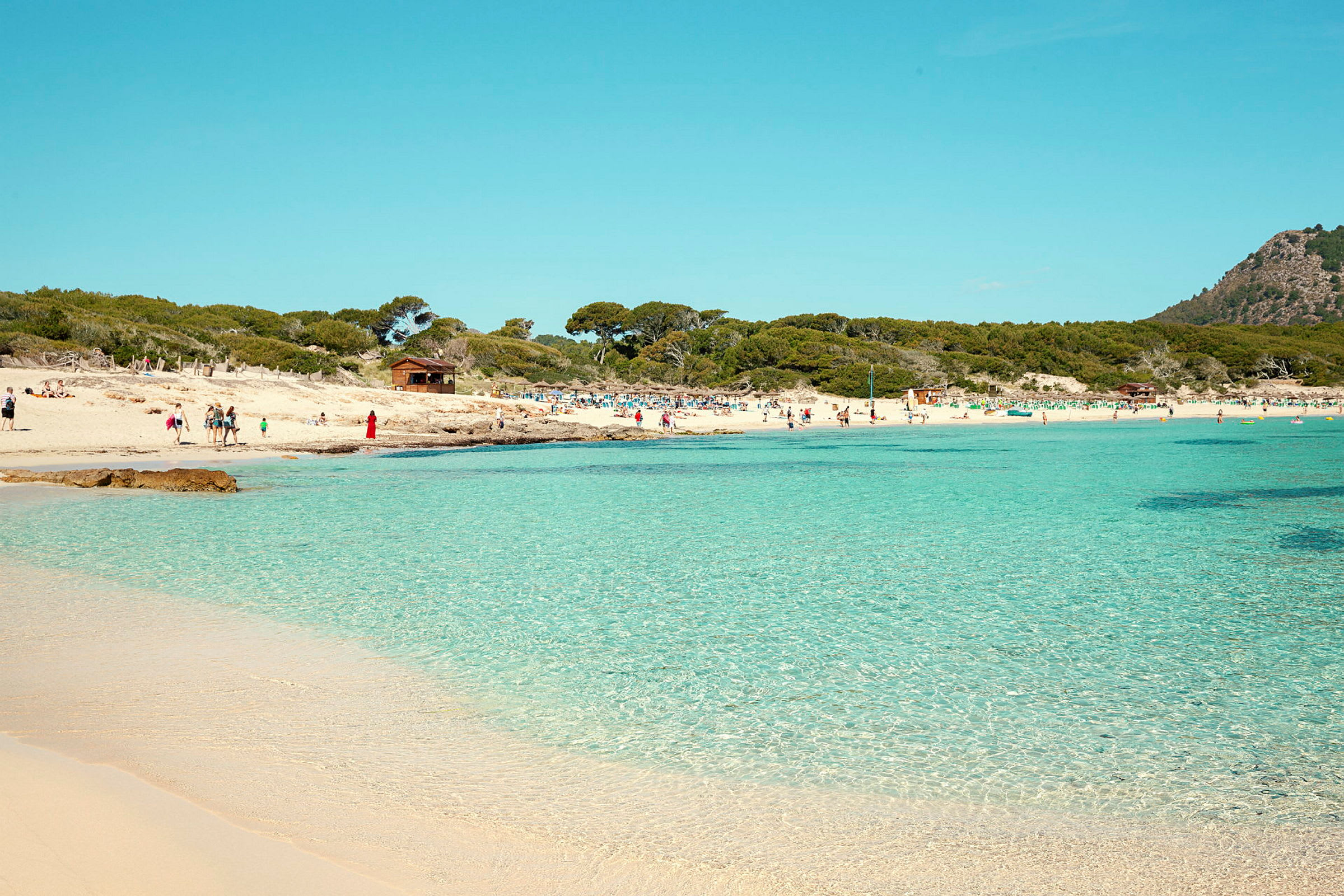 En strand med klart vand og mennesker der nyder solen. (AI-genereret tekst)