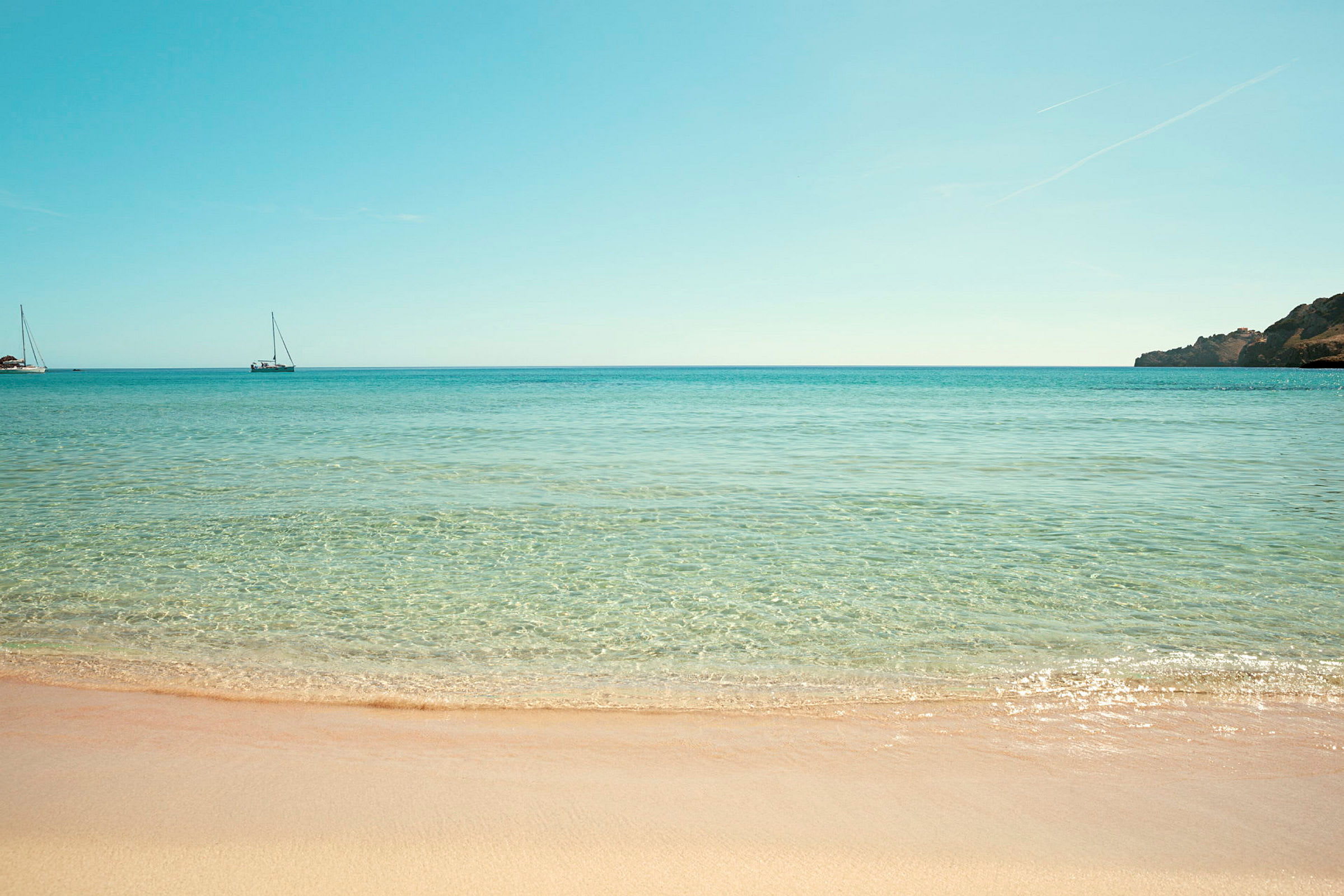 Strand med klart vand og to sejlbåde på havet. (AI-genereret tekst)
