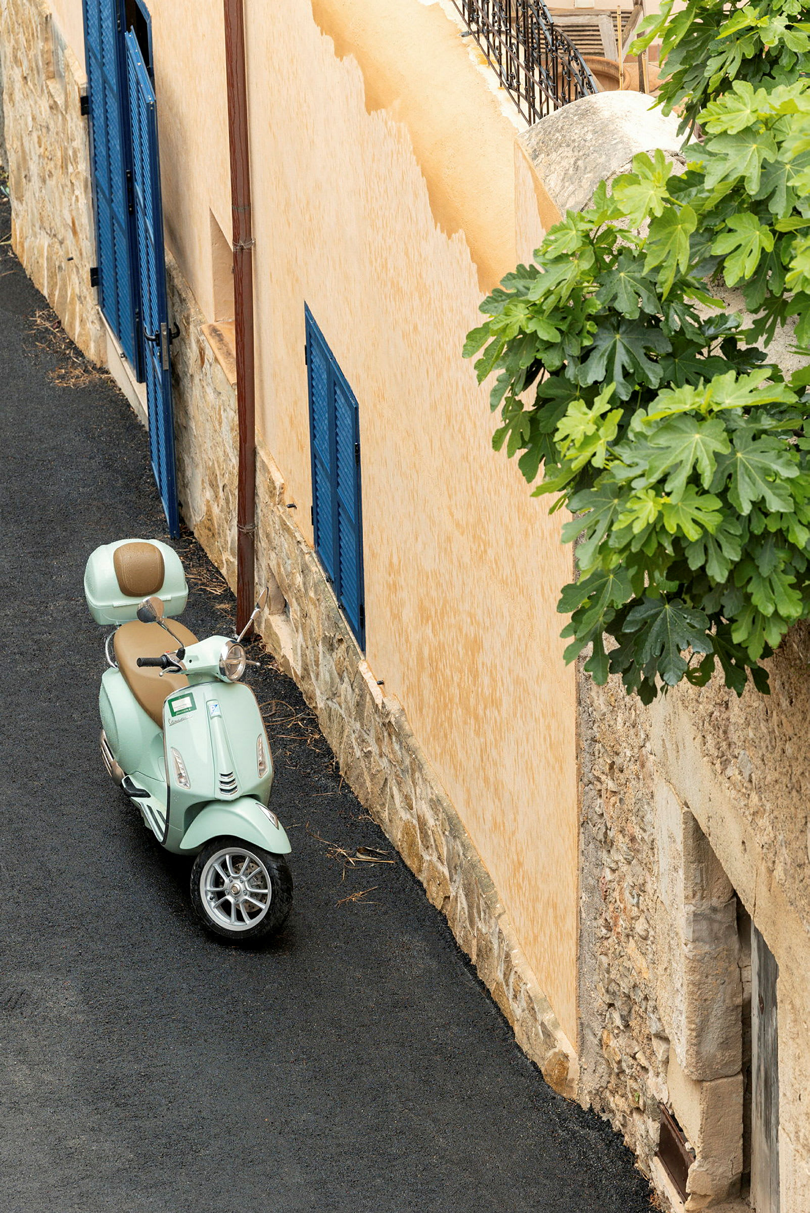 En lysegrøn scooter er parkeret ved en beige bygning med blå trævindueslåger. (AI-genereret tekst)
