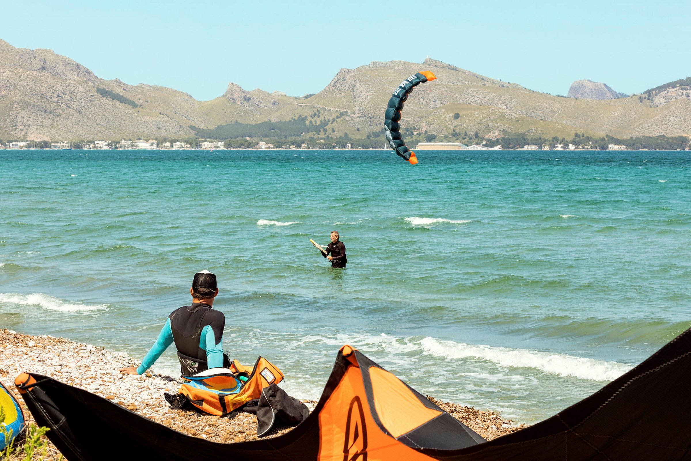 Person, der dyrker kitesurfing nær strandkanten med bjerge i baggrunden. (AI-genereret tekst)