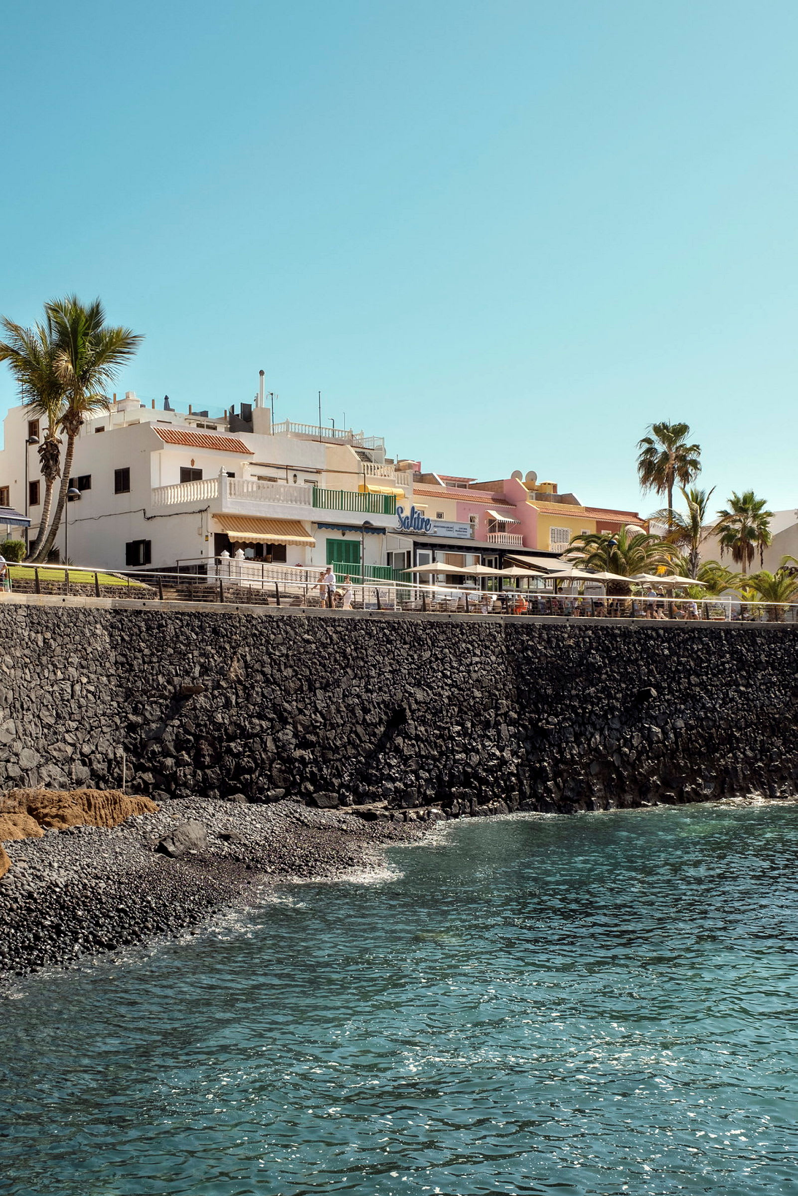 Strandpromenade med bygninger tæt på havet. (AI-genereret tekst)