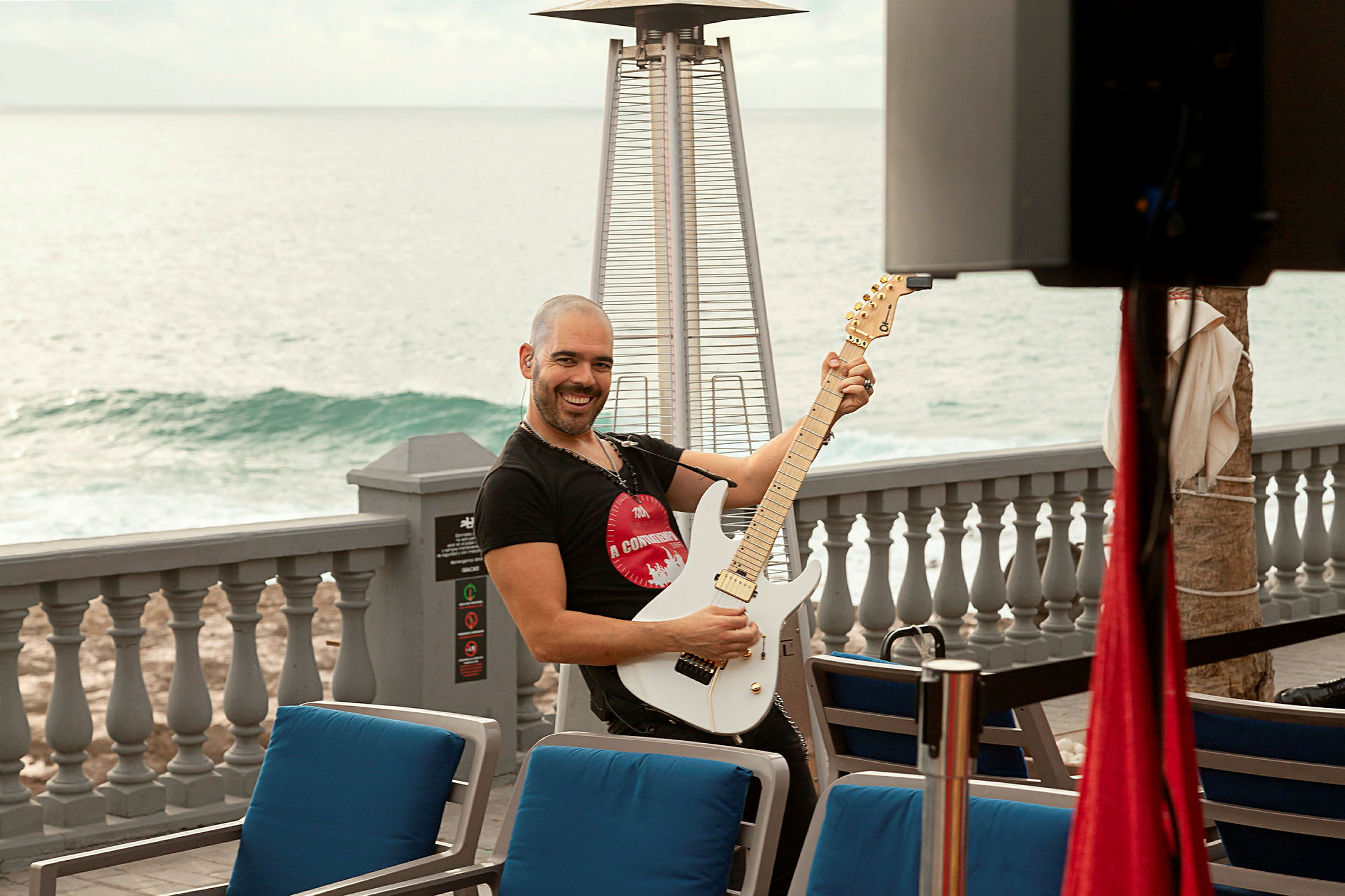 Person spiller elektrisk guitar ved en udendørs café med havet i baggrunden. (AI-genereret tekst)