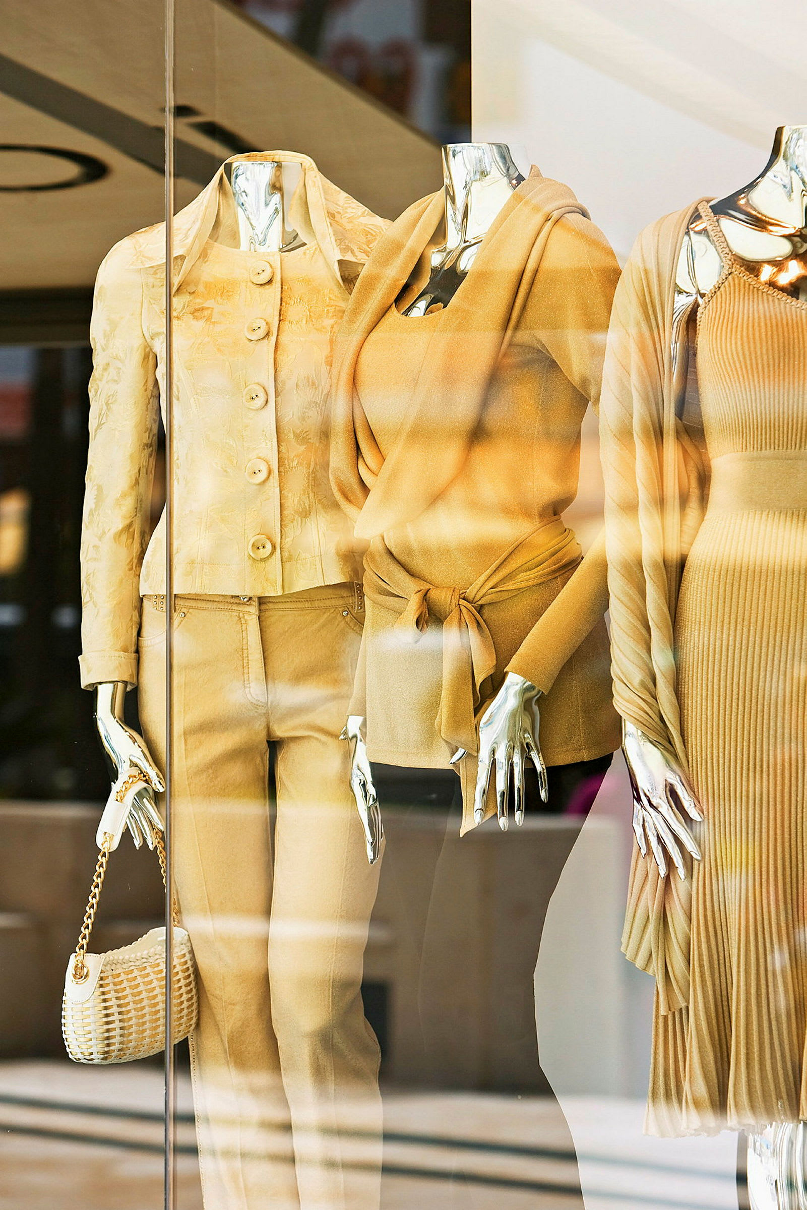 Et butiksvindue med tre mannequin-dukker klædt i elegante beige tøj. (AI-genereret tekst)