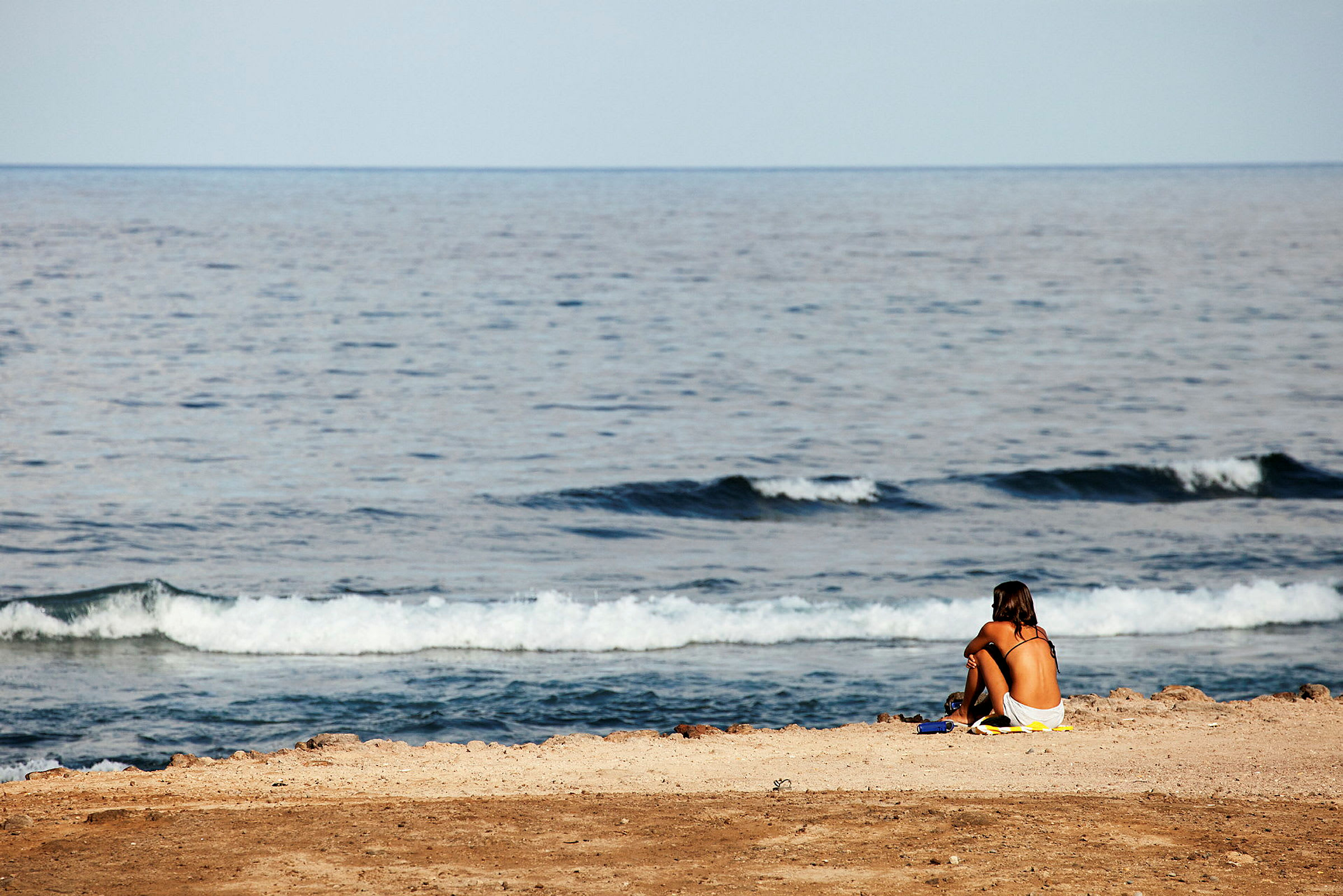 En person sidder på en strand nær havet. (AI-genereret tekst)