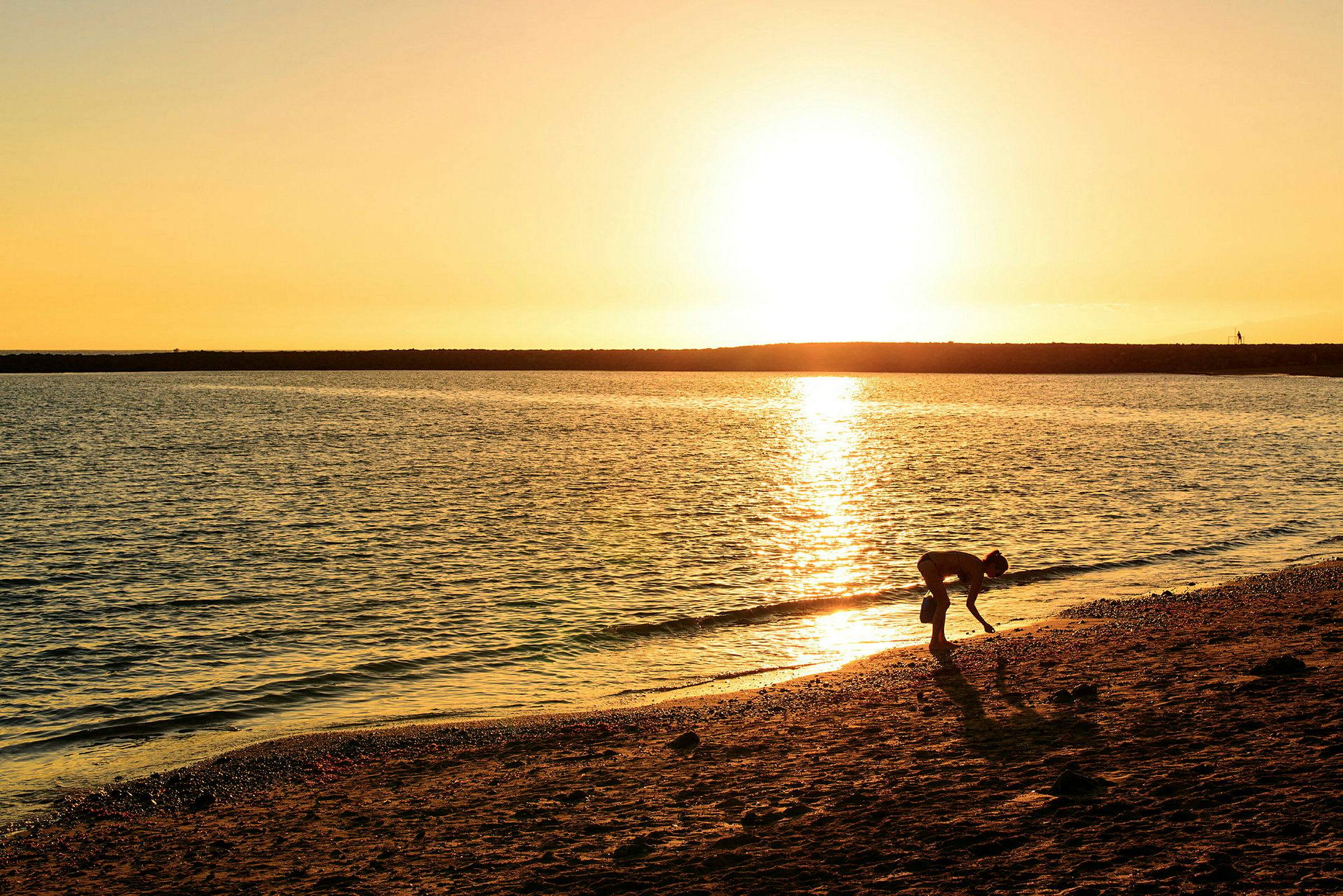 En person samler noget op ved stranden under solnedgangen. (AI-genereret tekst)
