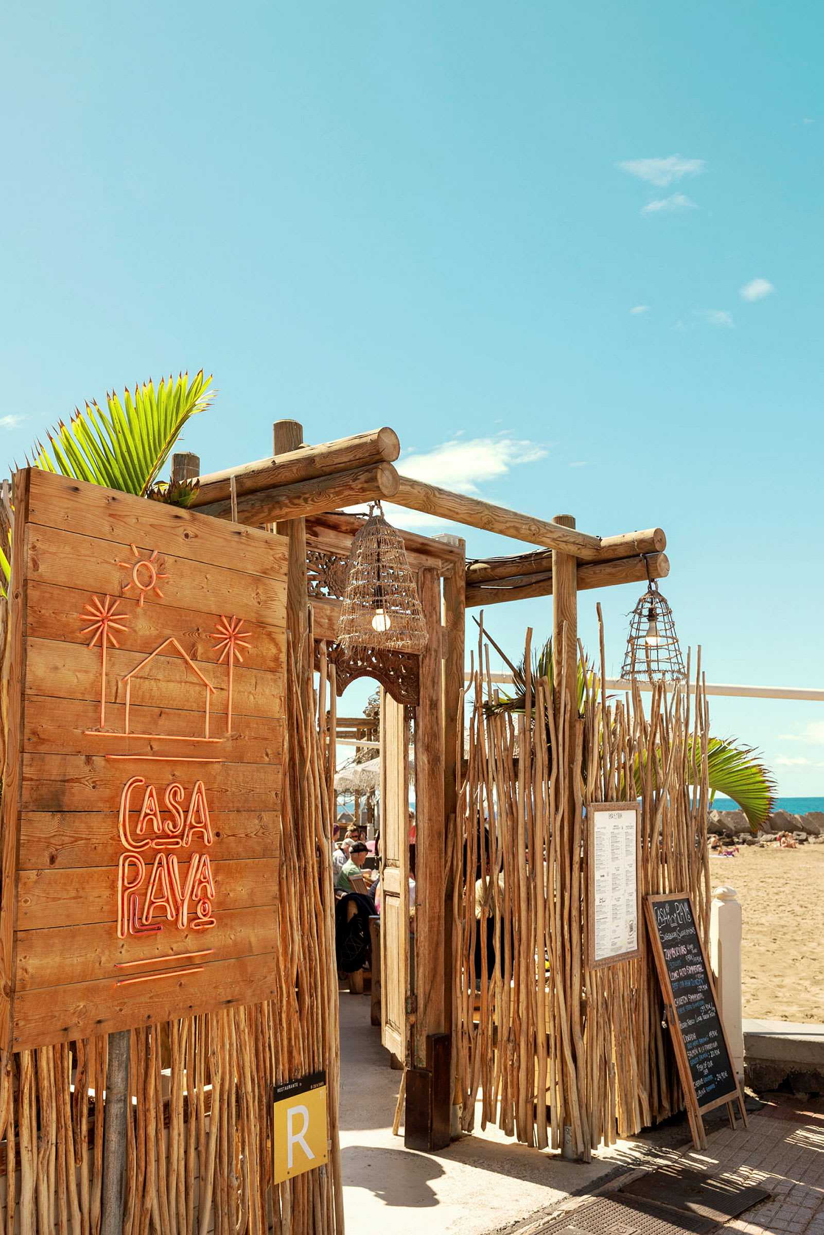 En strandrestaurant med trækonstruktion og neonskilt, der siger 'Casa Playa'. (AI-genereret tekst)