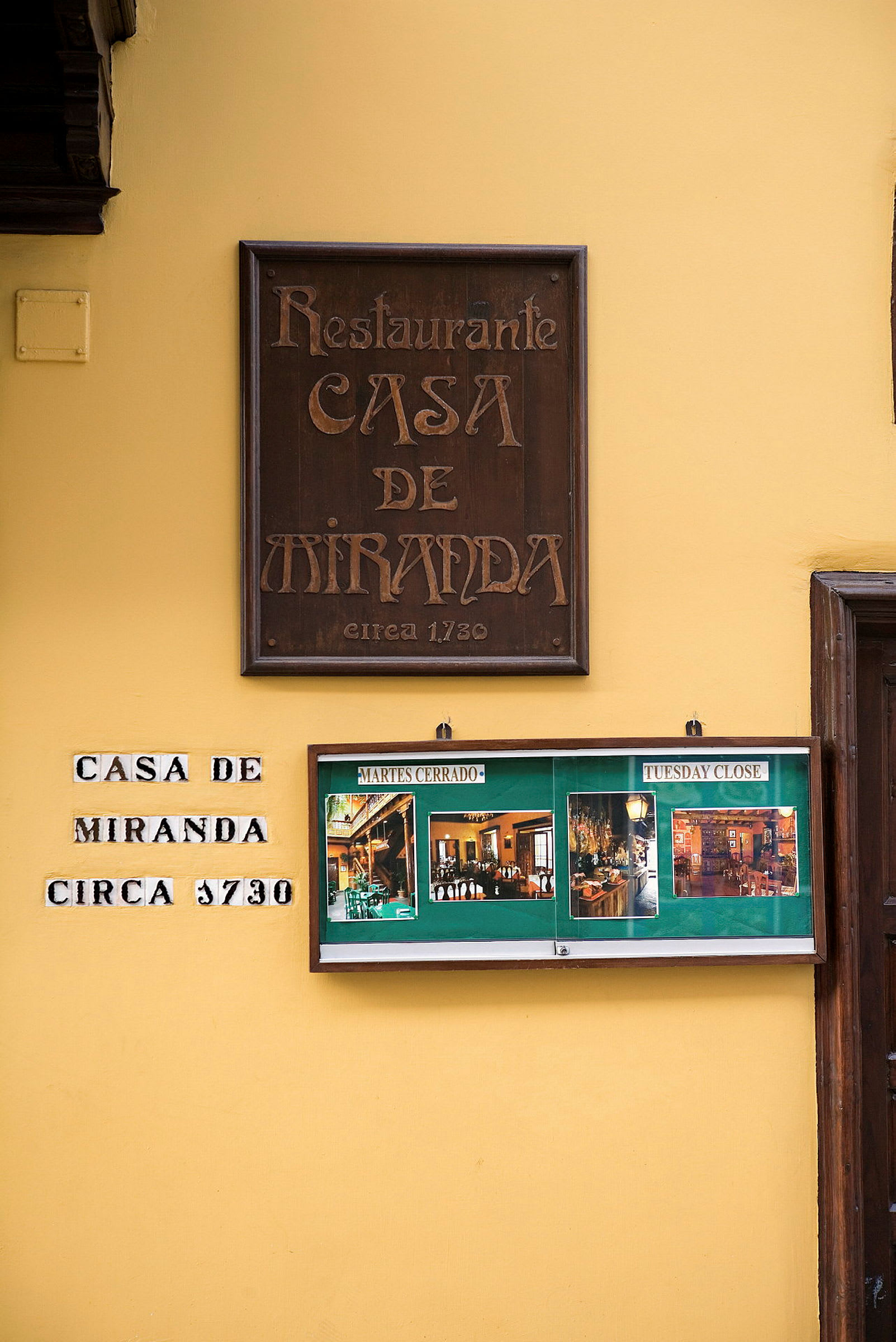 Gul væg med skiltet til restauranten "Casa de Miranda" og billeder af interiør. (AI-genereret tekst)
