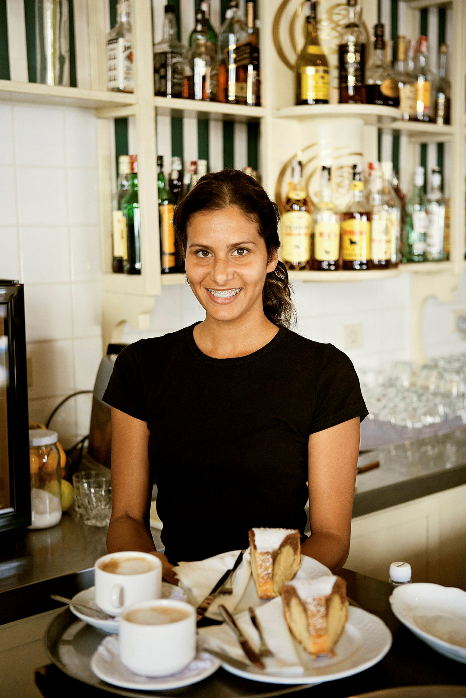 En serveringsbakke med to kopper kaffe og to stykker kage placeret på et bord foran en bar. (AI-genereret tekst)