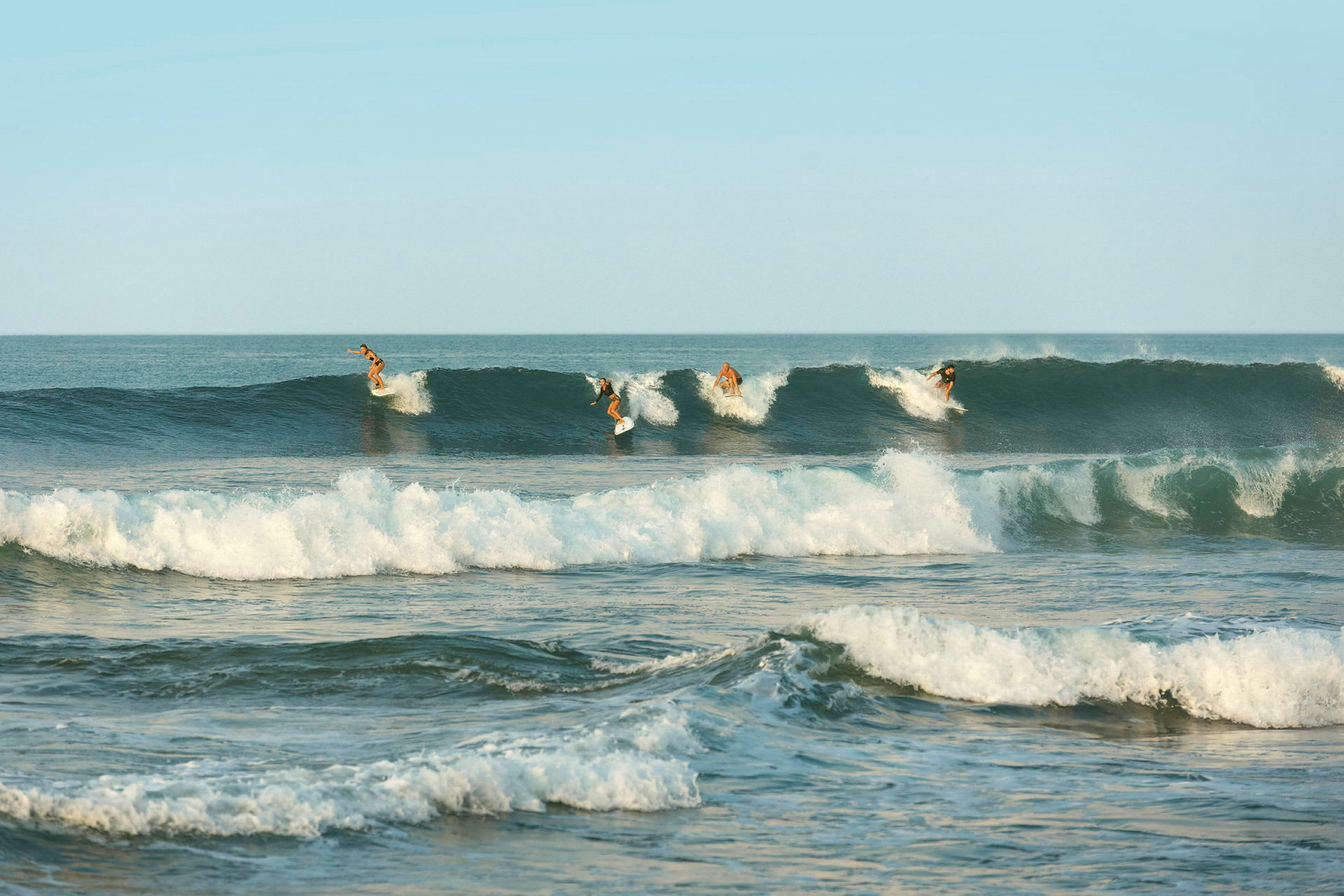 Fire surfere surfer på bølger i havet under en klar himmel. (AI-genereret tekst)