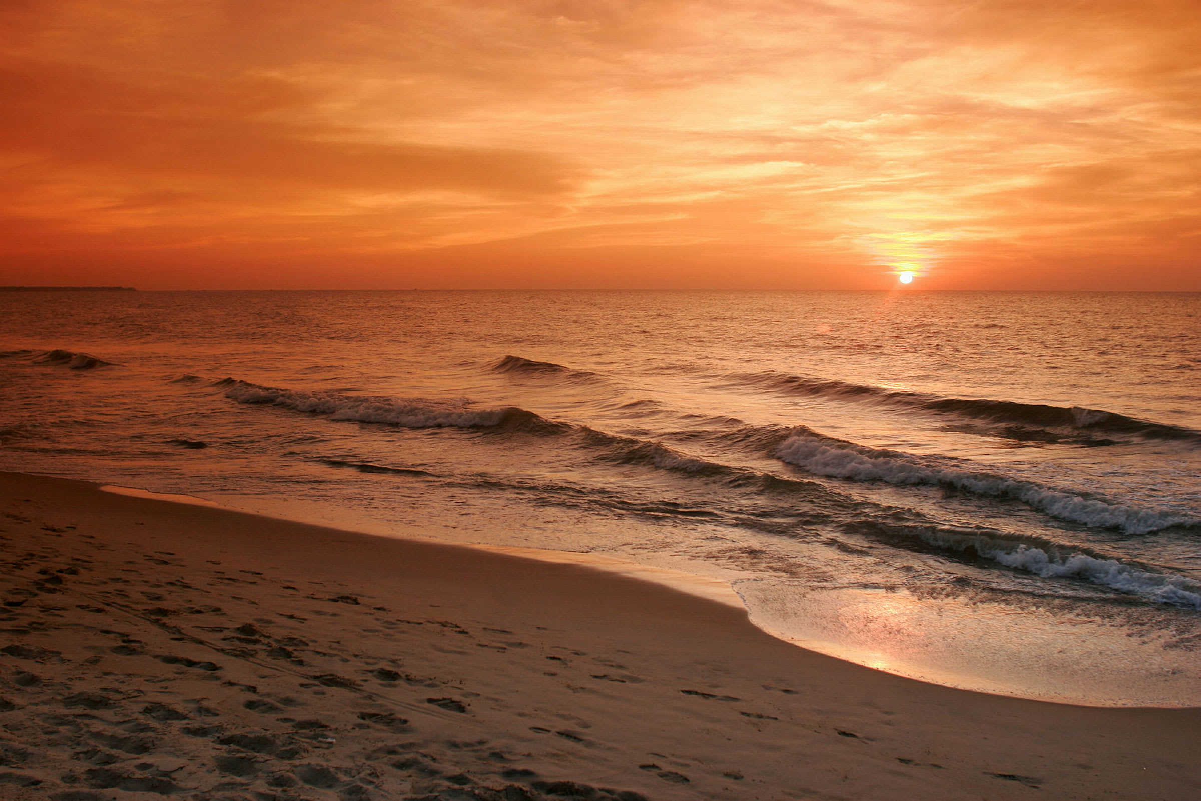 Billede der viser en strand ved havet med bølger og en solnedgang. (AI-genereret tekst)