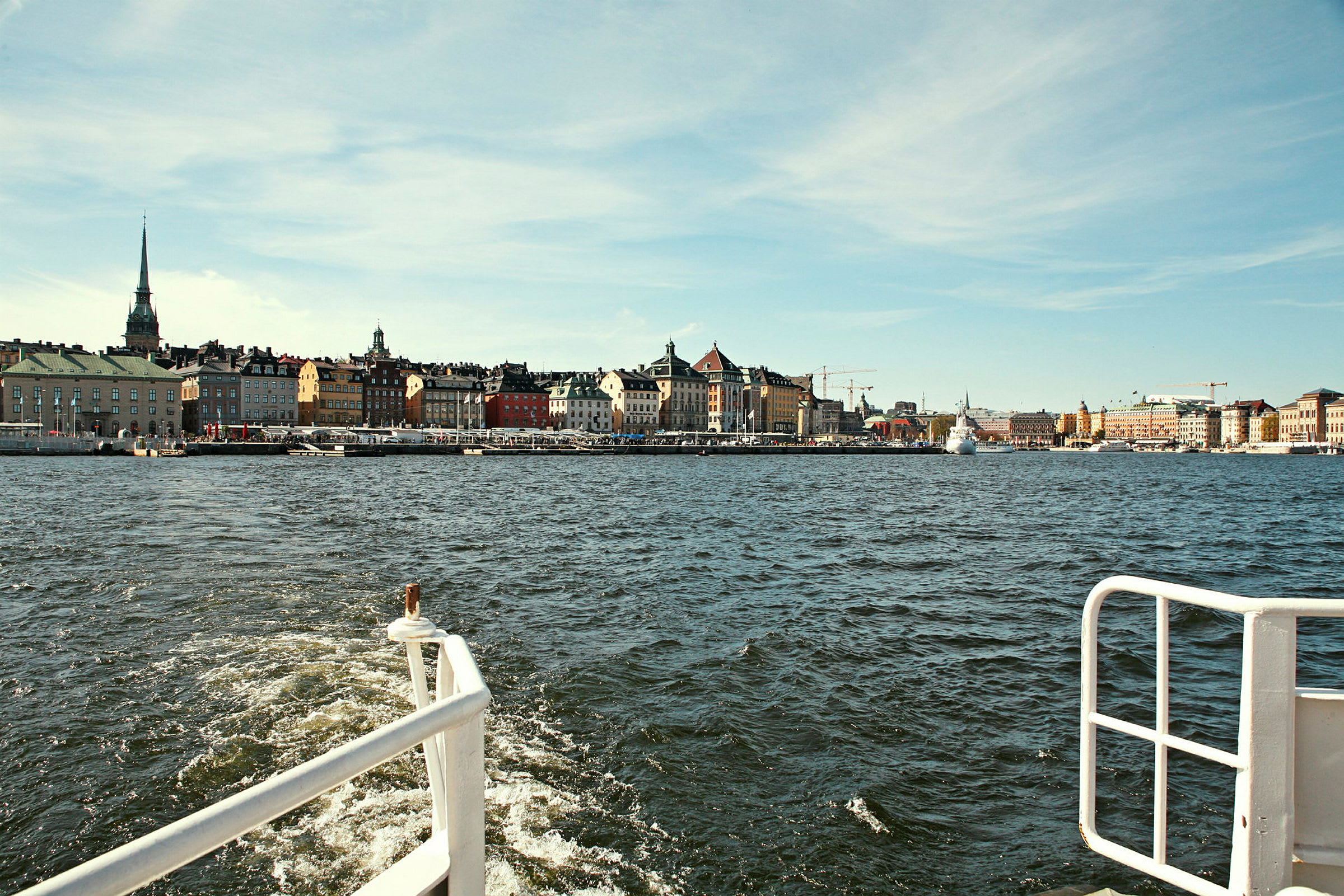 Udsigt fra en båd med en bypromenade og farverige bygninger langs vandet. (AI-genereret tekst)
