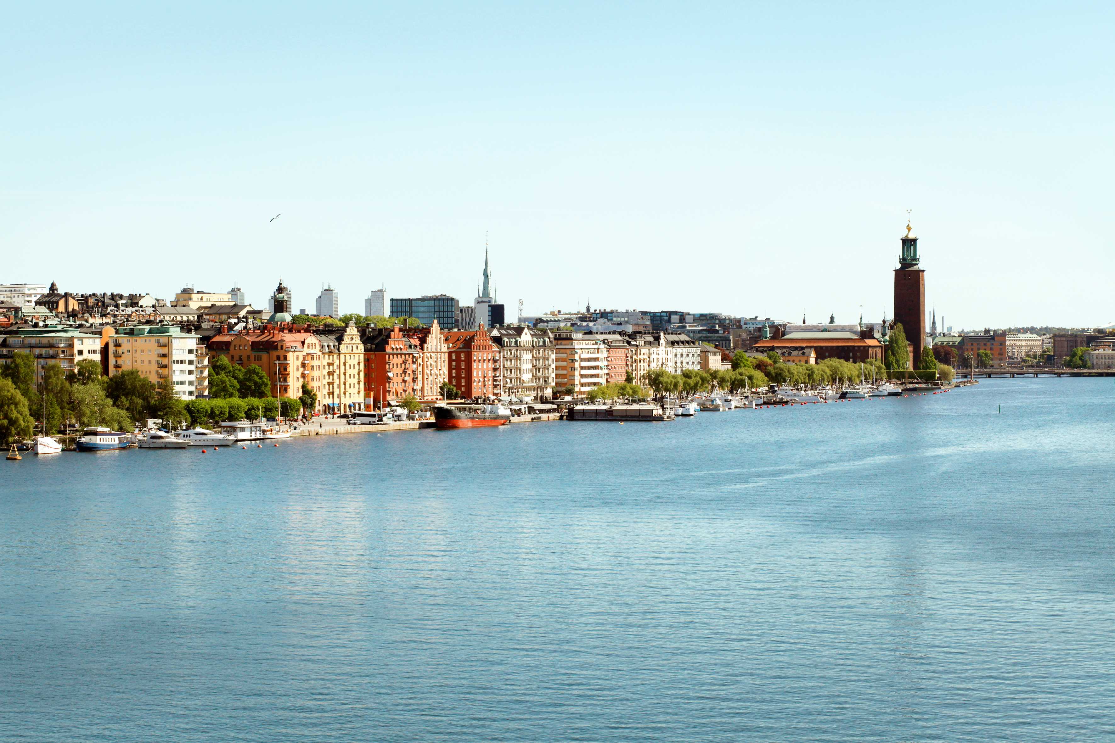 Bymiljø ved en vandspejl med bygninger og både i forgrunden. (AI-genereret tekst)
