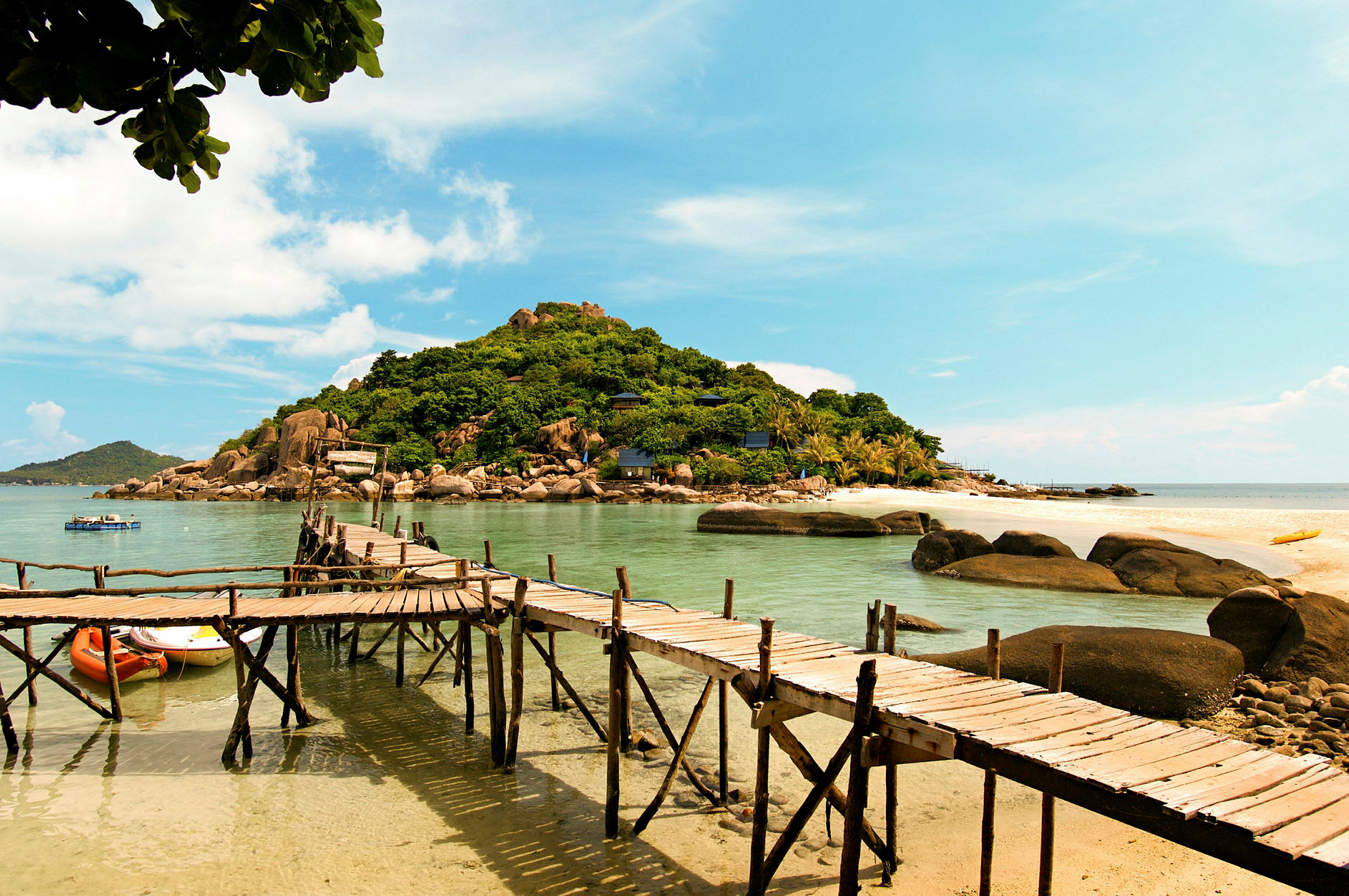 En udsigt til en træbro, der strækker sig over klart vand med en bakke dækket af vegetation i baggrunden. (AI-genereret tekst)