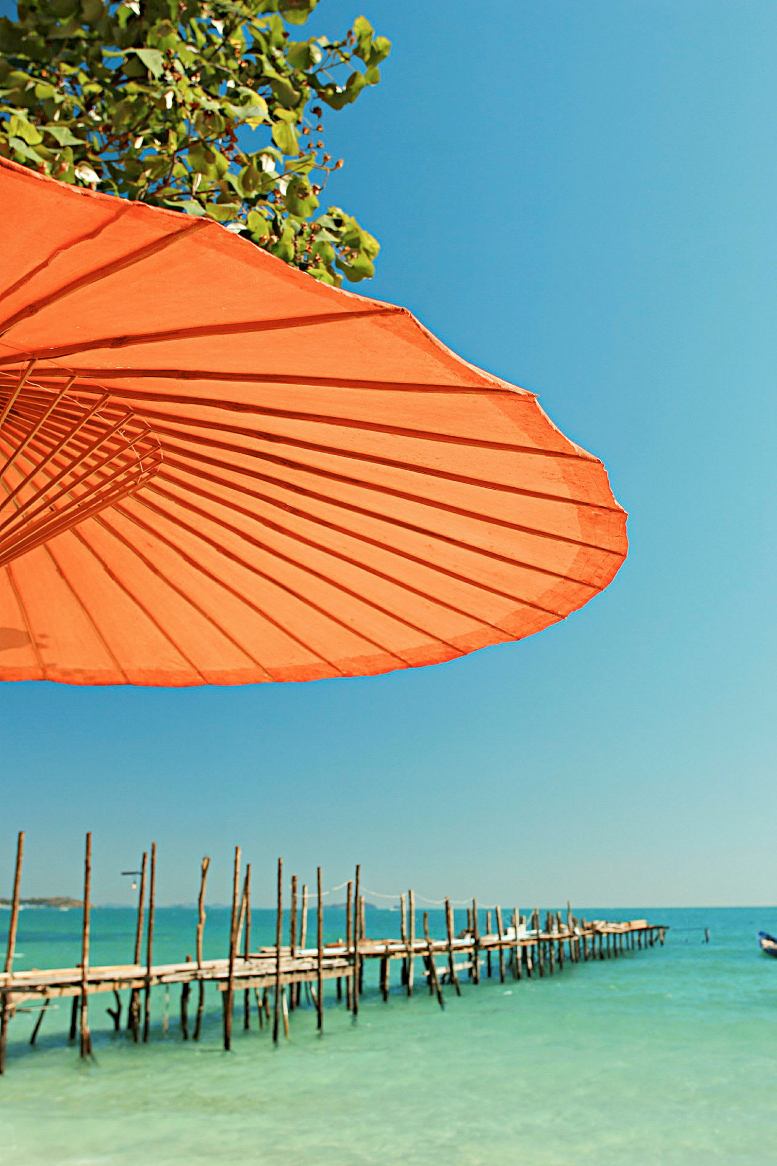 Orange parasol med udsigt over havet og en mole. (AI-genereret tekst)
