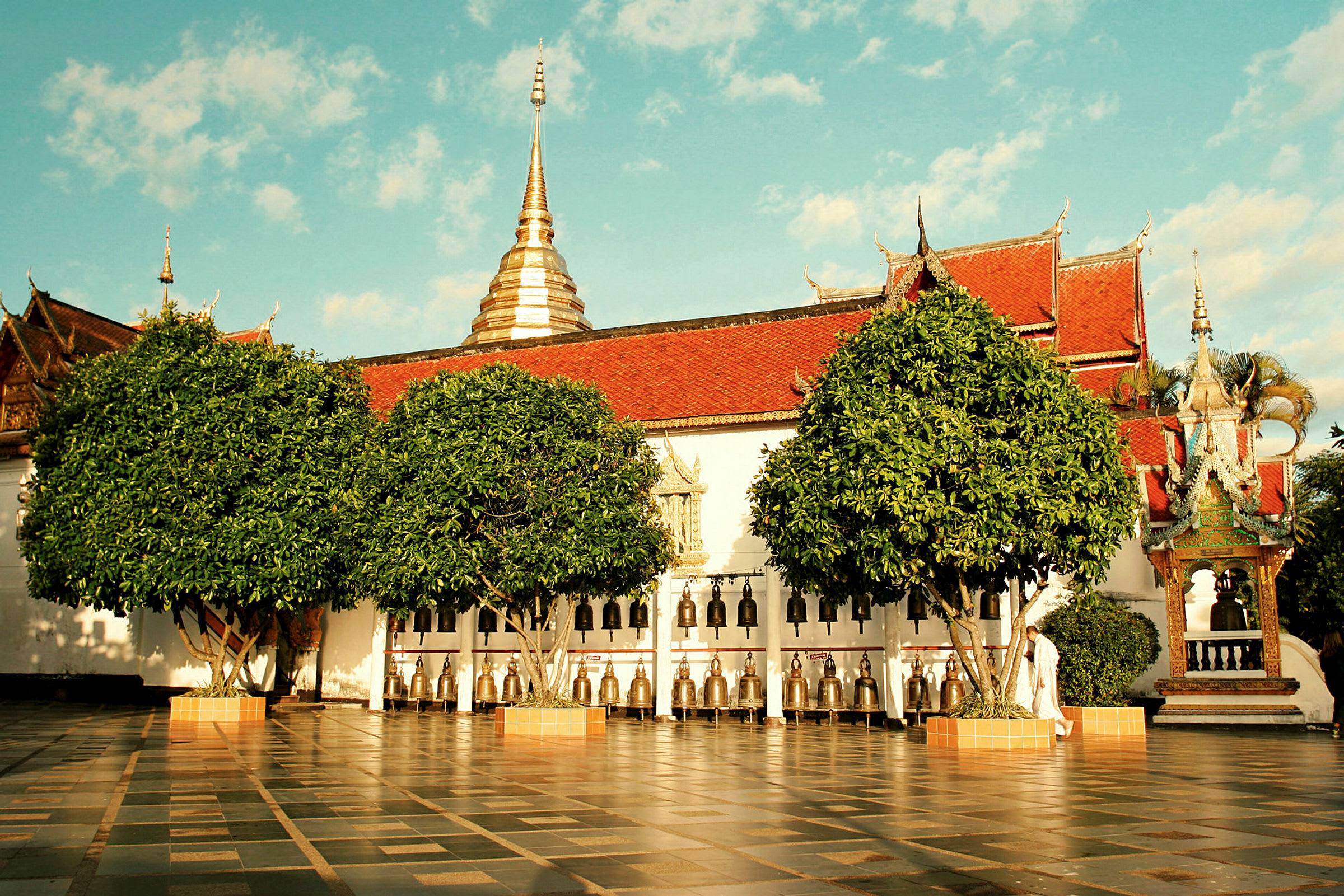 Billede af et buddhistisk tempel med klokker og frodige træer. (AI-genereret tekst)