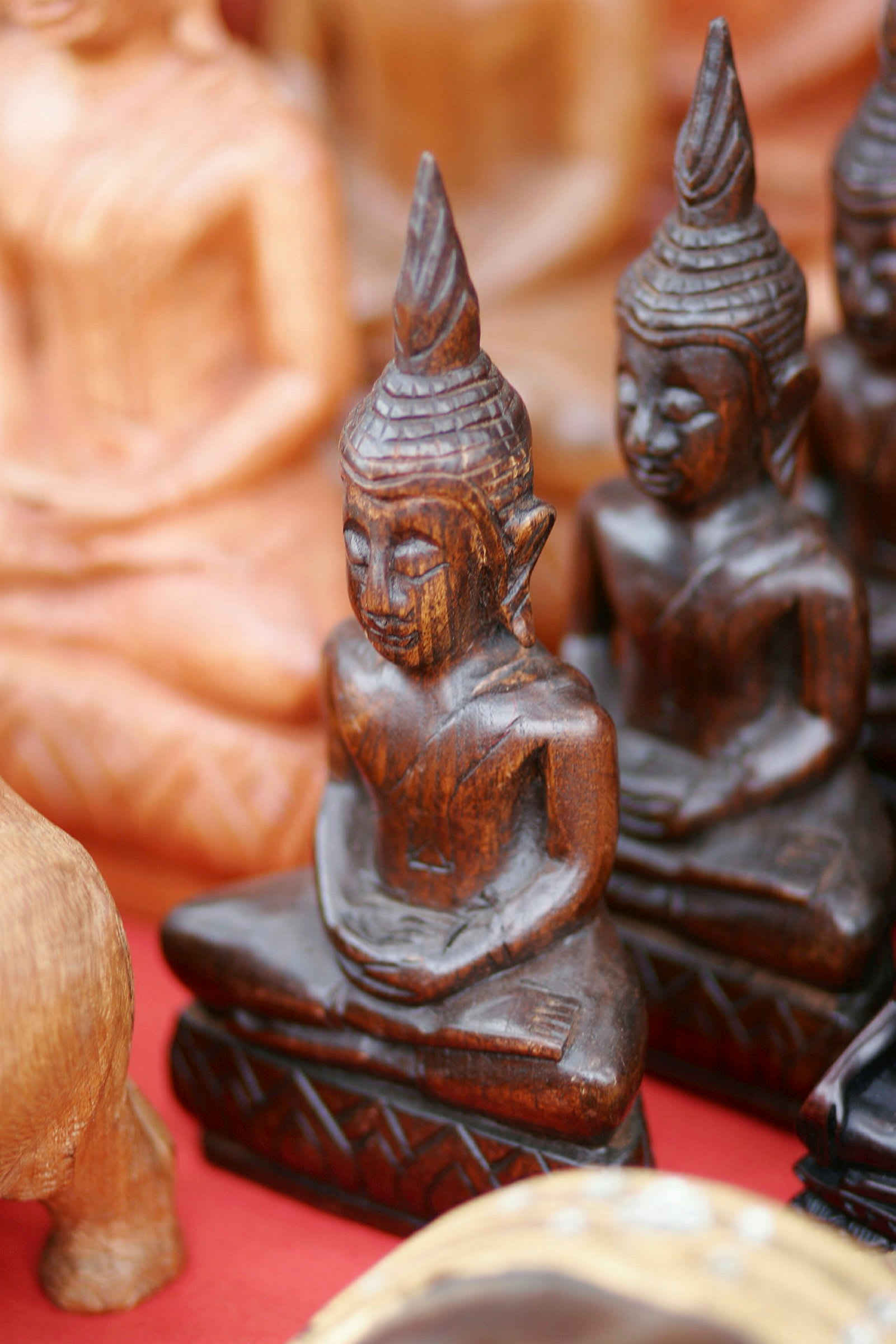 Billede af en samling små, træudskårne buddhastatuer foran en rød baggrund. (AI-genereret tekst)