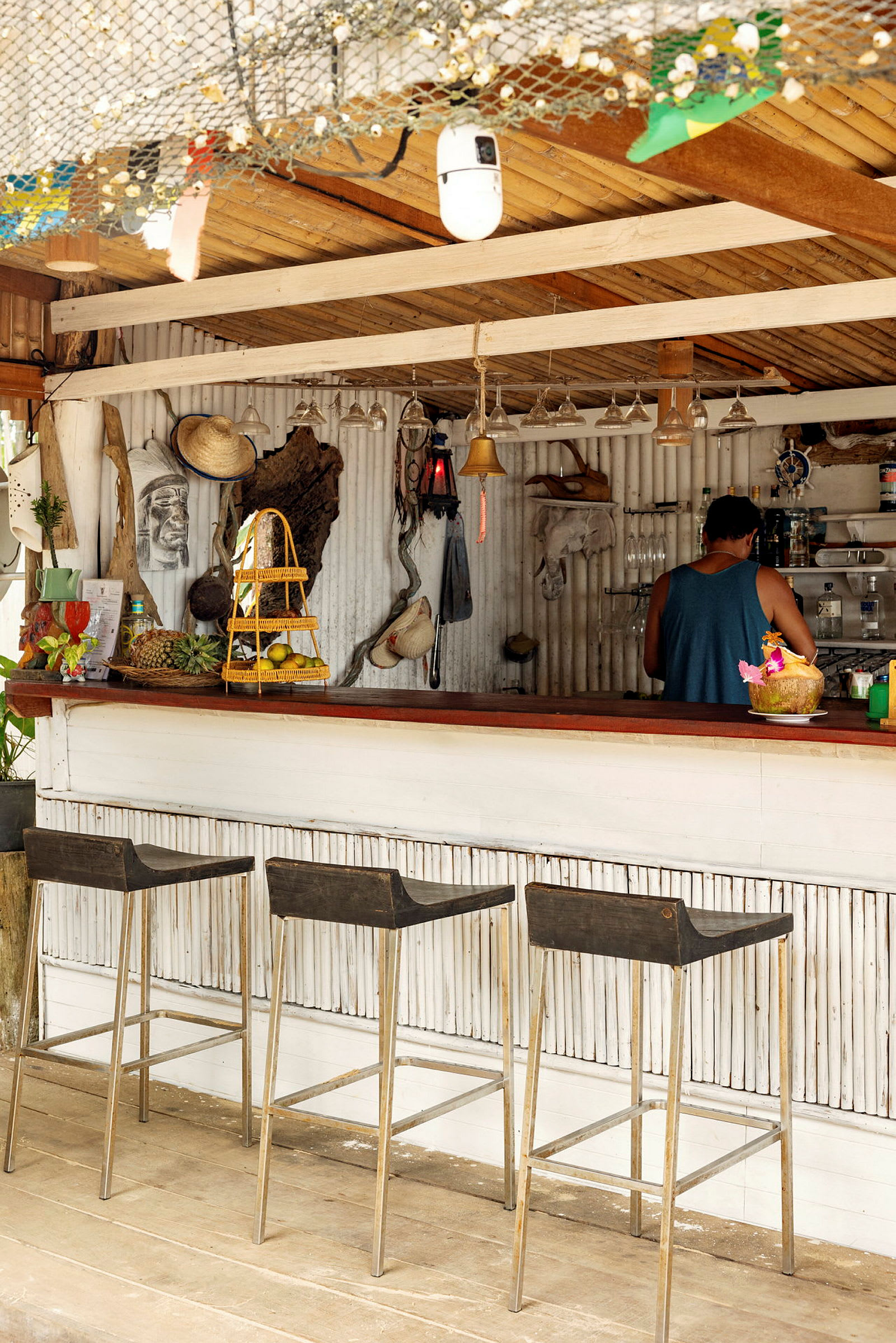 Billede af en strandbar med tre skamler, dekorationer på væggen og en person ved disken. (AI-genereret tekst)