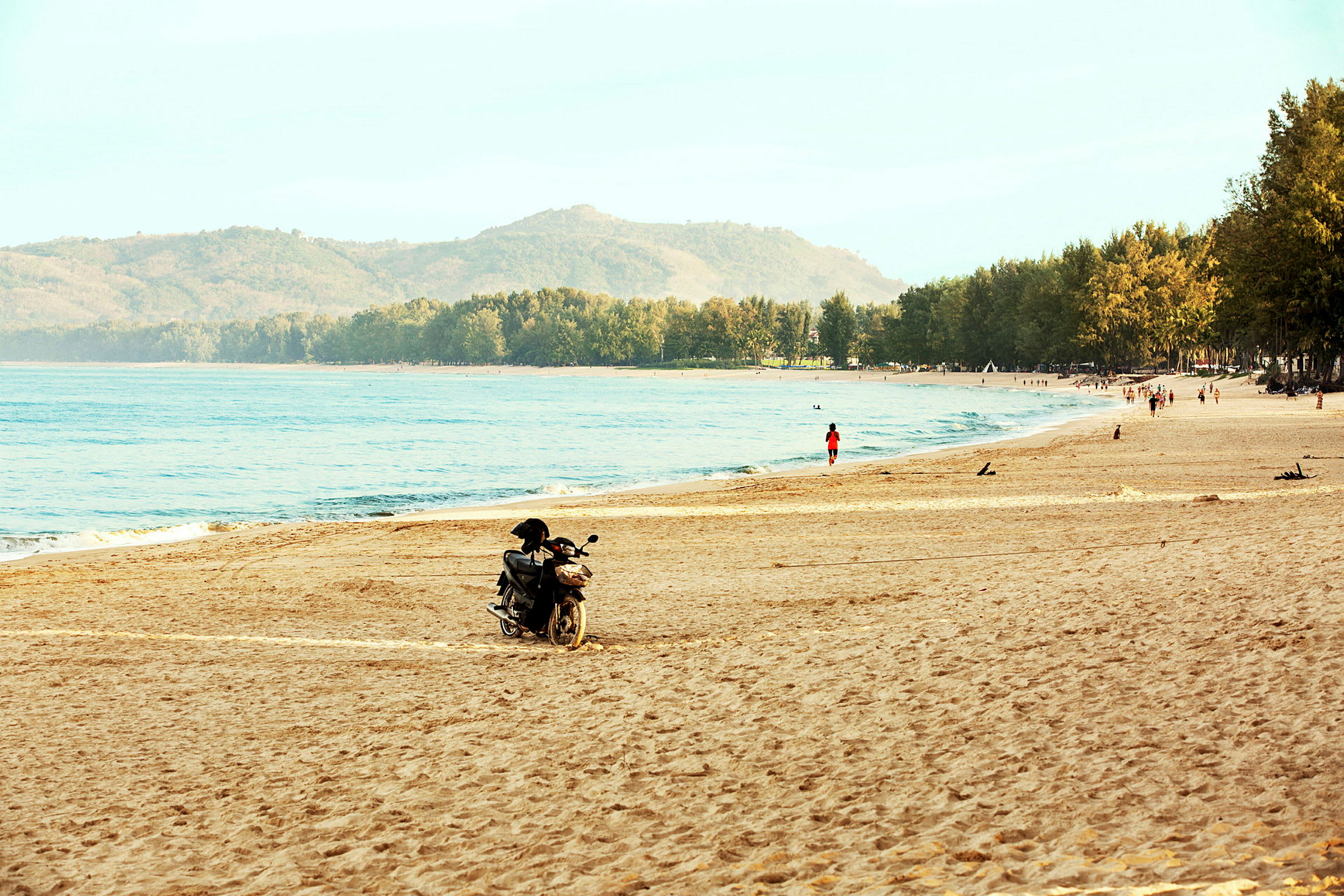 En strand med sand, havet og en motorcykel. En person går tæt på vandet. (AI-genereret tekst)