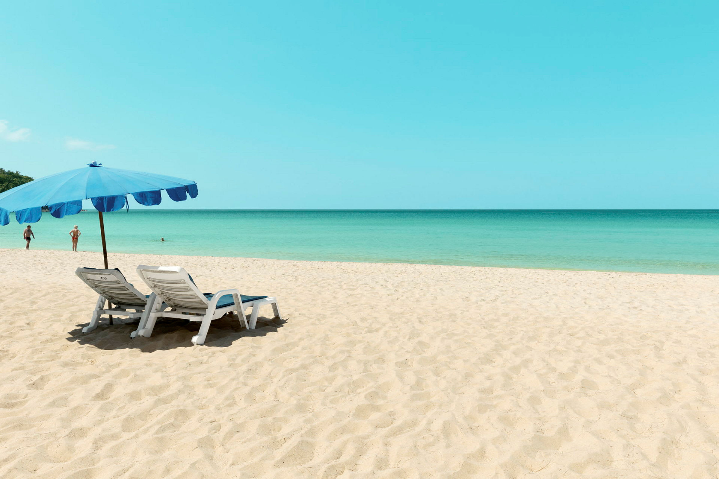 To solsenge under en blå parasol på en sandstrand med havet i baggrunden. (AI-genereret tekst)