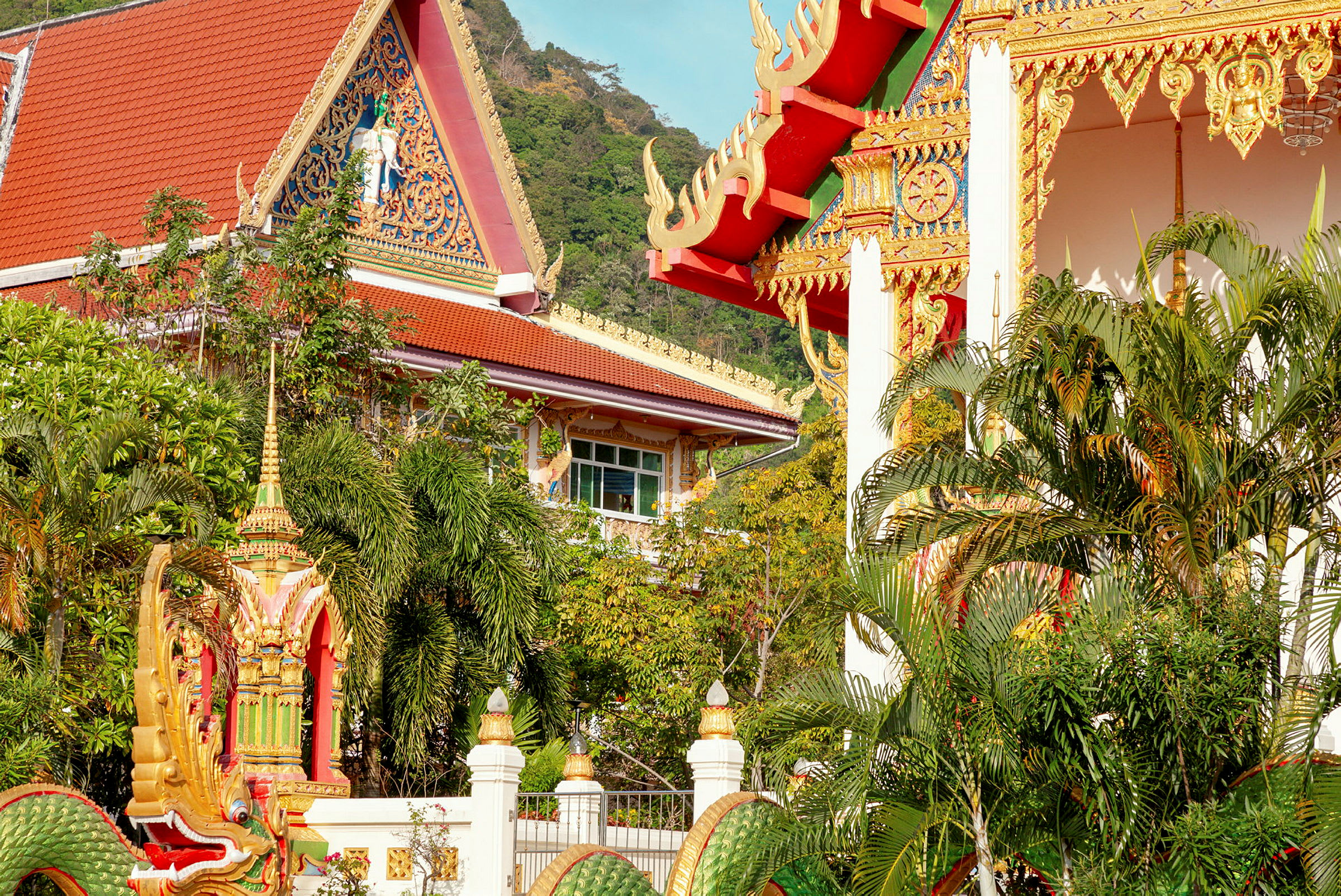 Billede af en traditionel thailandsk bygning med dekorative detaljer omgivet af frodig vegetation. (AI-genereret tekst)