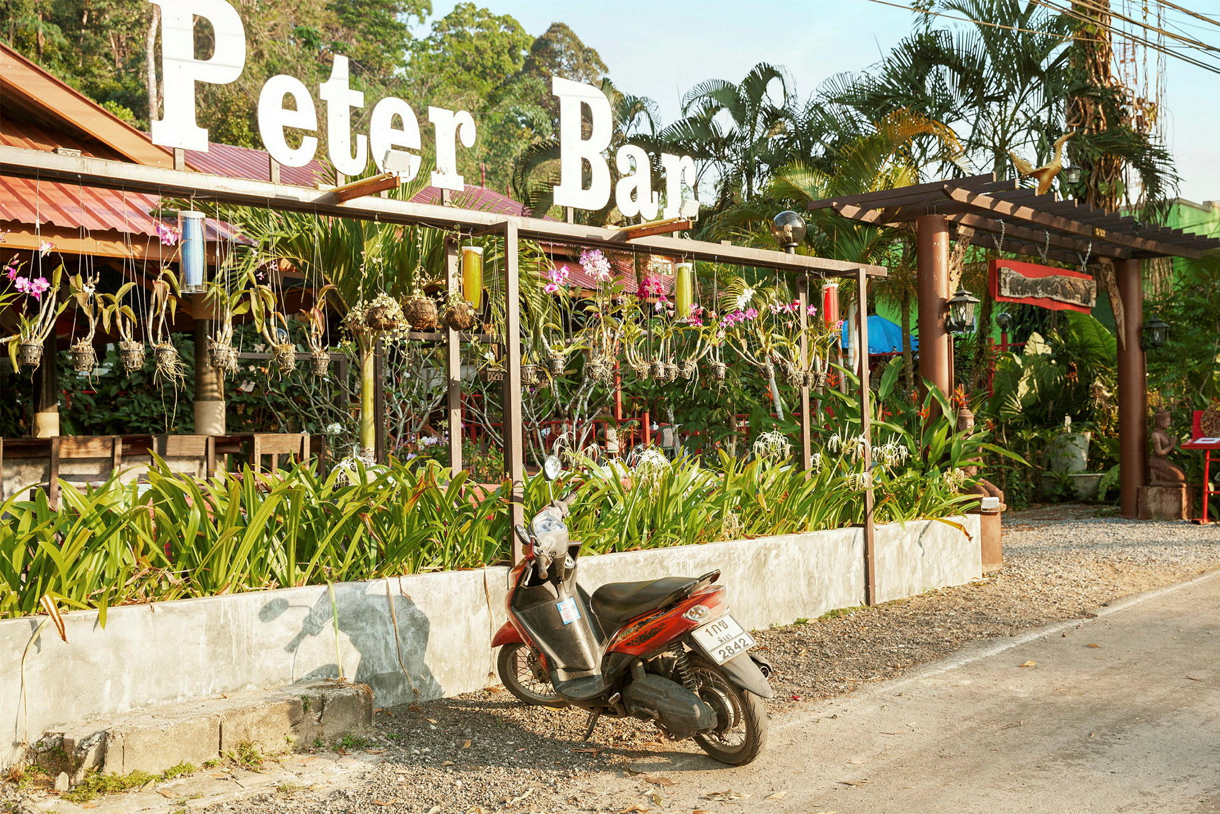 En motorcykel parkeret foran en restaurant med skilte og beplantning. (AI-genereret tekst)