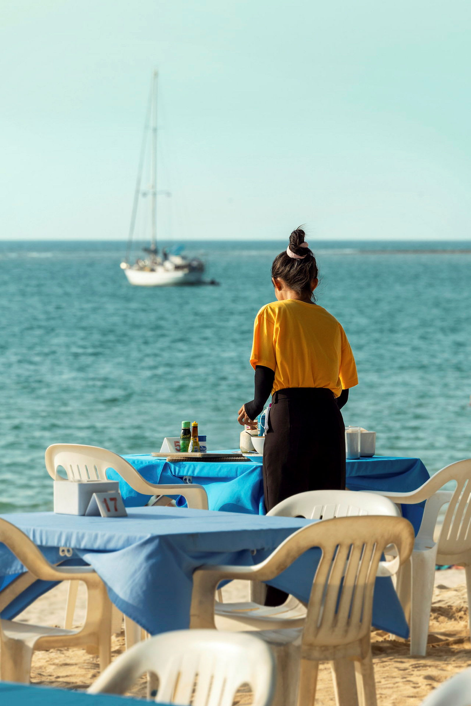 En person ordner borde på en restaurant med udsigt over havet. (AI-genereret tekst)