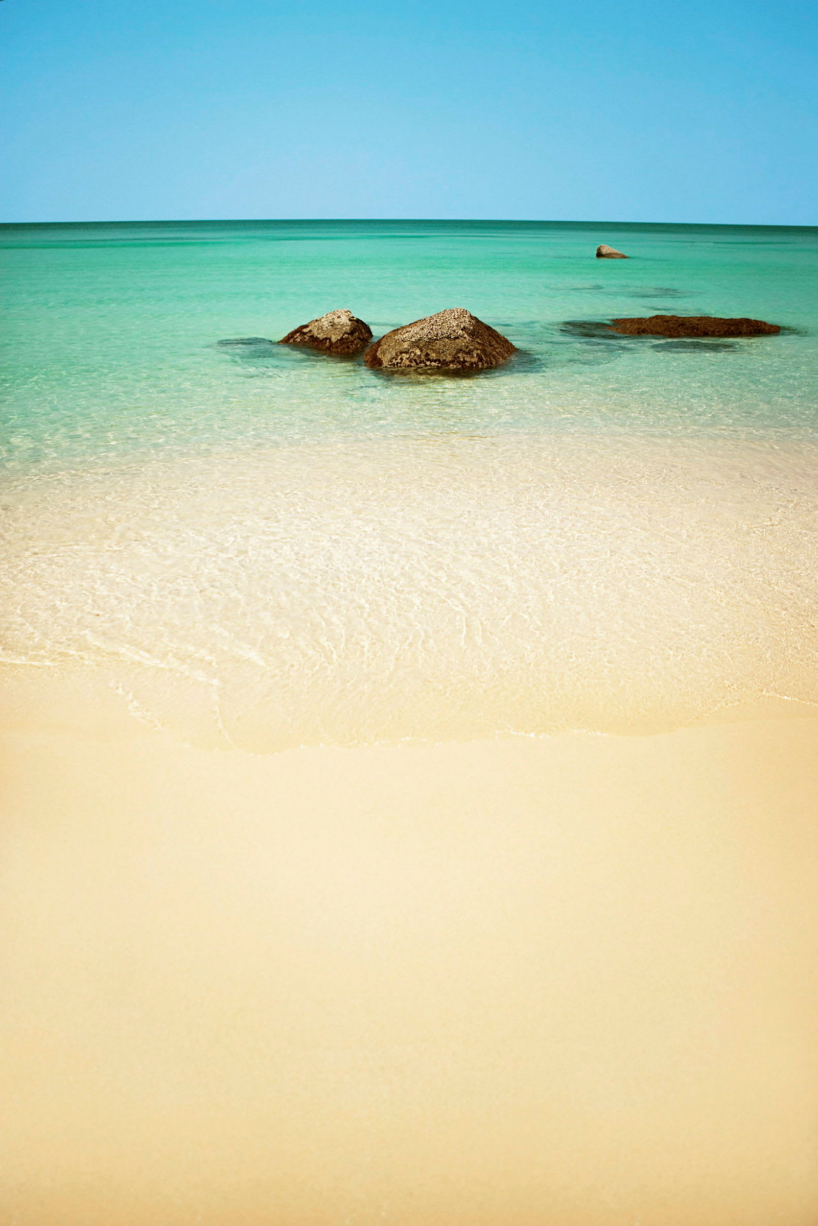 En sandstrand med klart vand og nogle synlige sten i havet. (AI-genereret tekst)