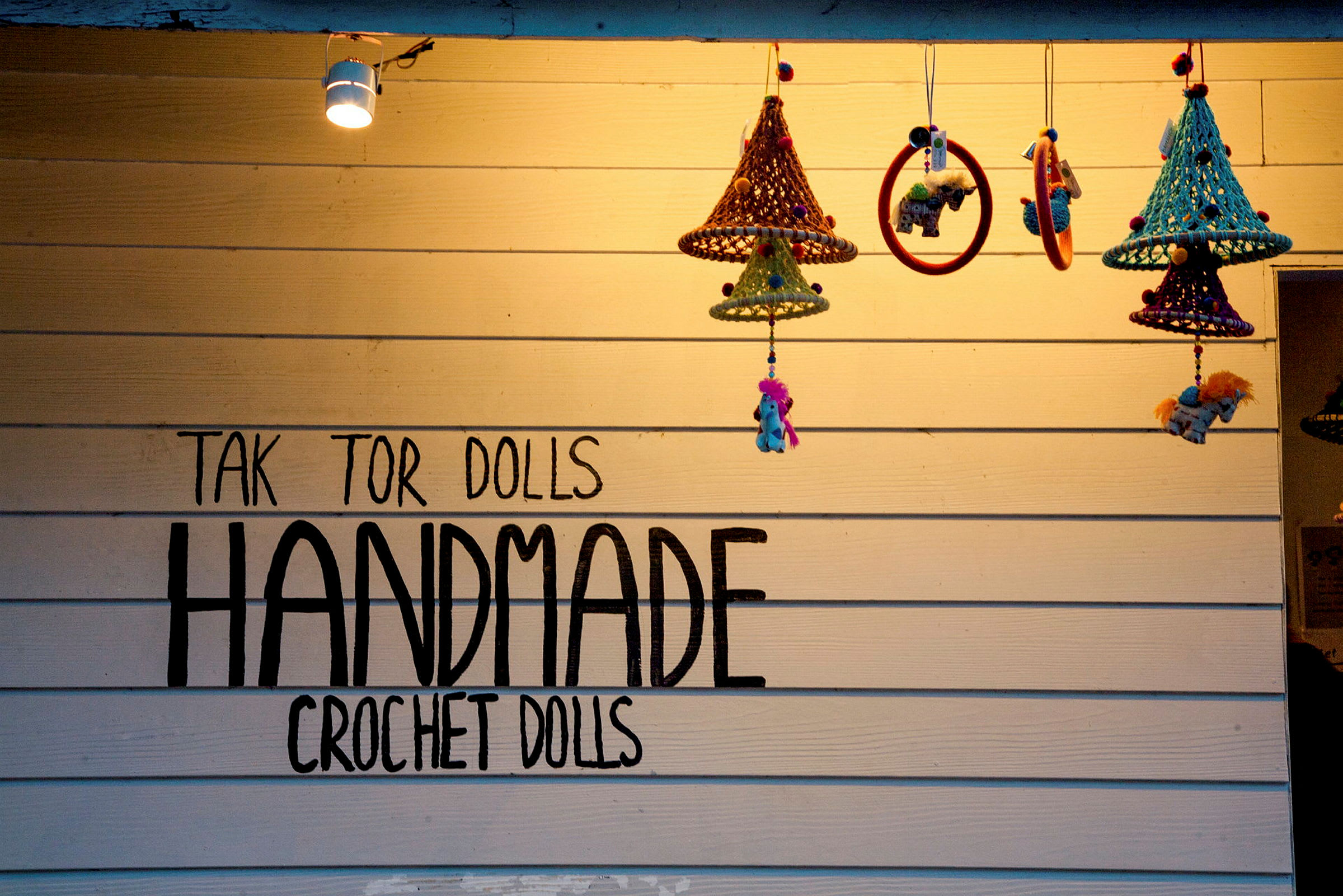 Væg med teksten 'Handmade Crochet Dolls' og hængende hæklede dekorationer. (AI-genereret tekst)