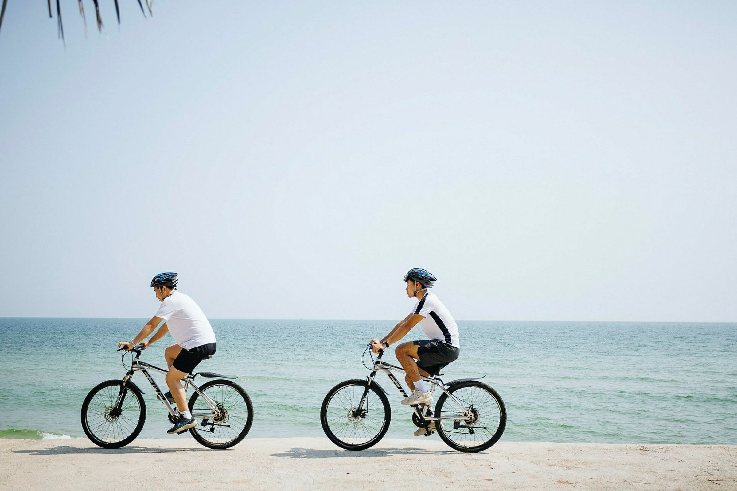 To personer cykler langs en strand nær havet. (AI-genereret tekst)