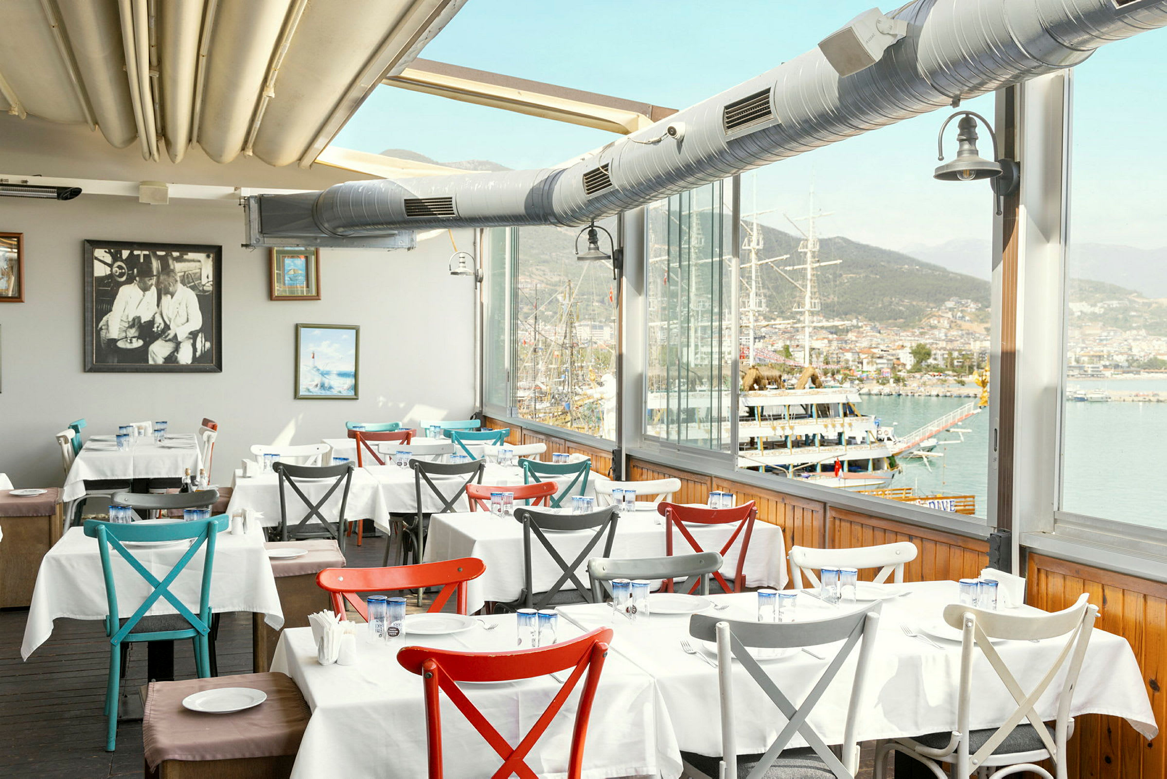 Interiør af en restaurant med dækkede borde og udsigt over havnen. (AI-genereret tekst)