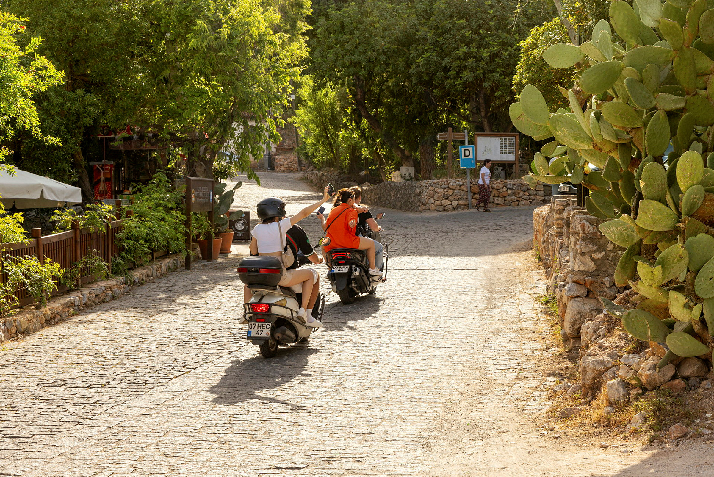 Personer der kører på scootere på en belagt vej omgivet af grønne områder. (AI-genereret tekst)