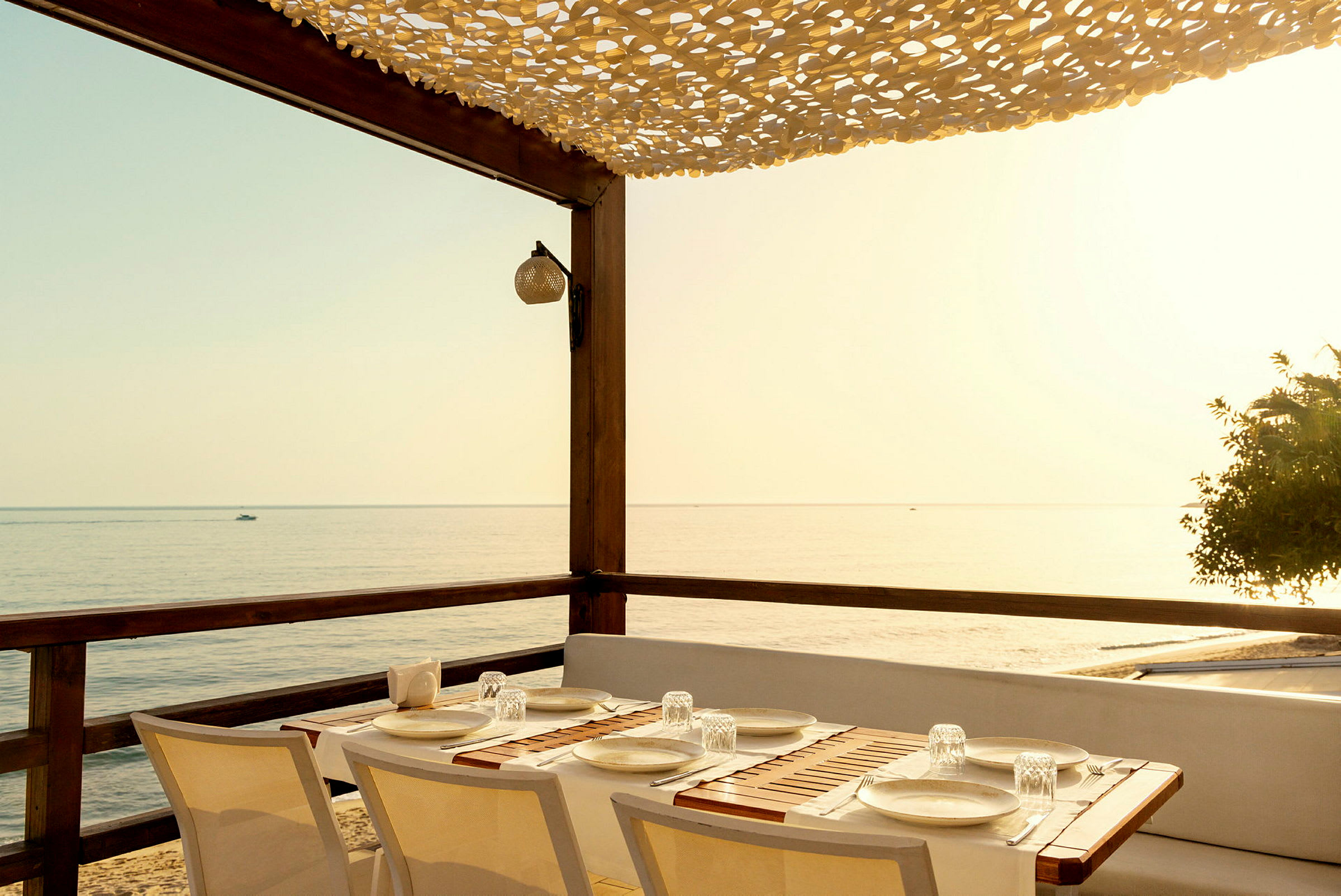 Et bord med opdækning på en terrasse ved havet under et skyggefuldt tag. (AI-genereret tekst)