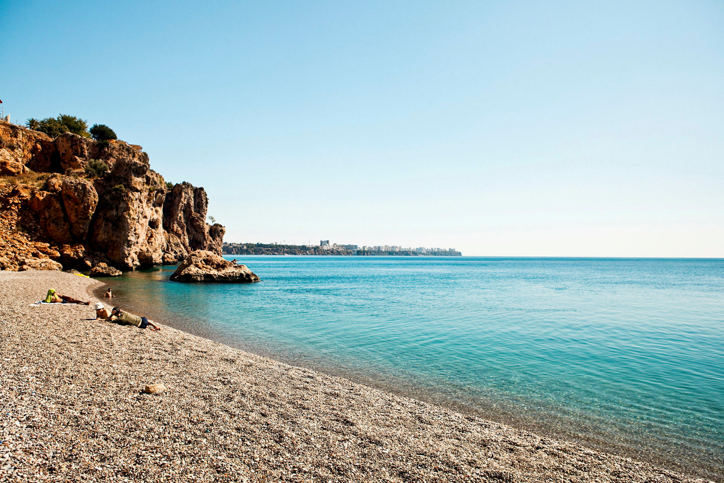 Sandstrand med klipper ved havet under klar himmel. (AI-genereret tekst)