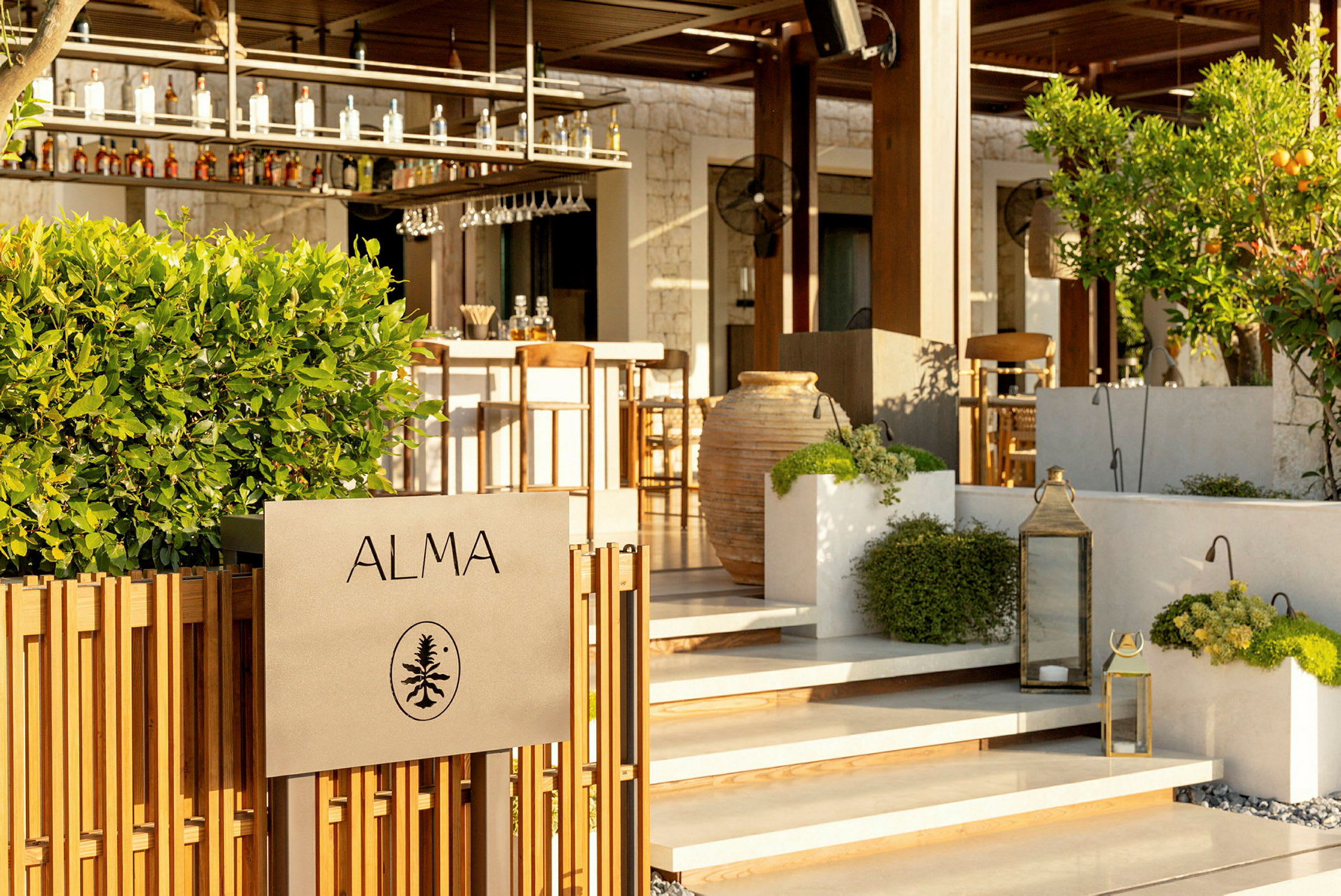 Skilt med teksten "ALMA" foran en bar med grønne planter og dekorationer. (AI-genereret tekst)