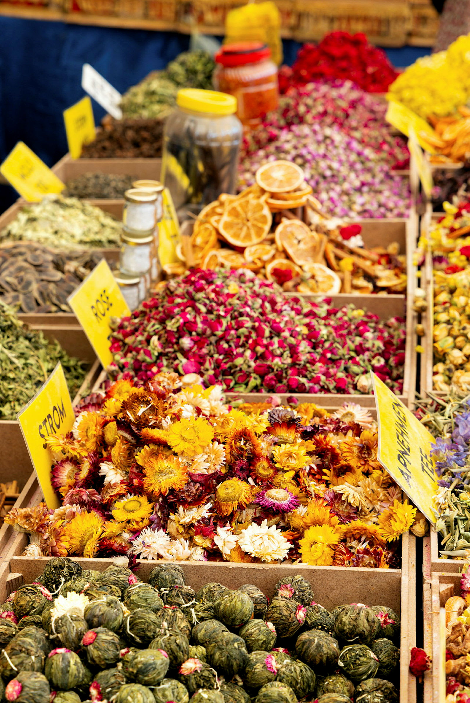 Nærbillede af diverse krydderier, urter og tørrede blomster i kasser på en markedsplads. (AI-genereret tekst)