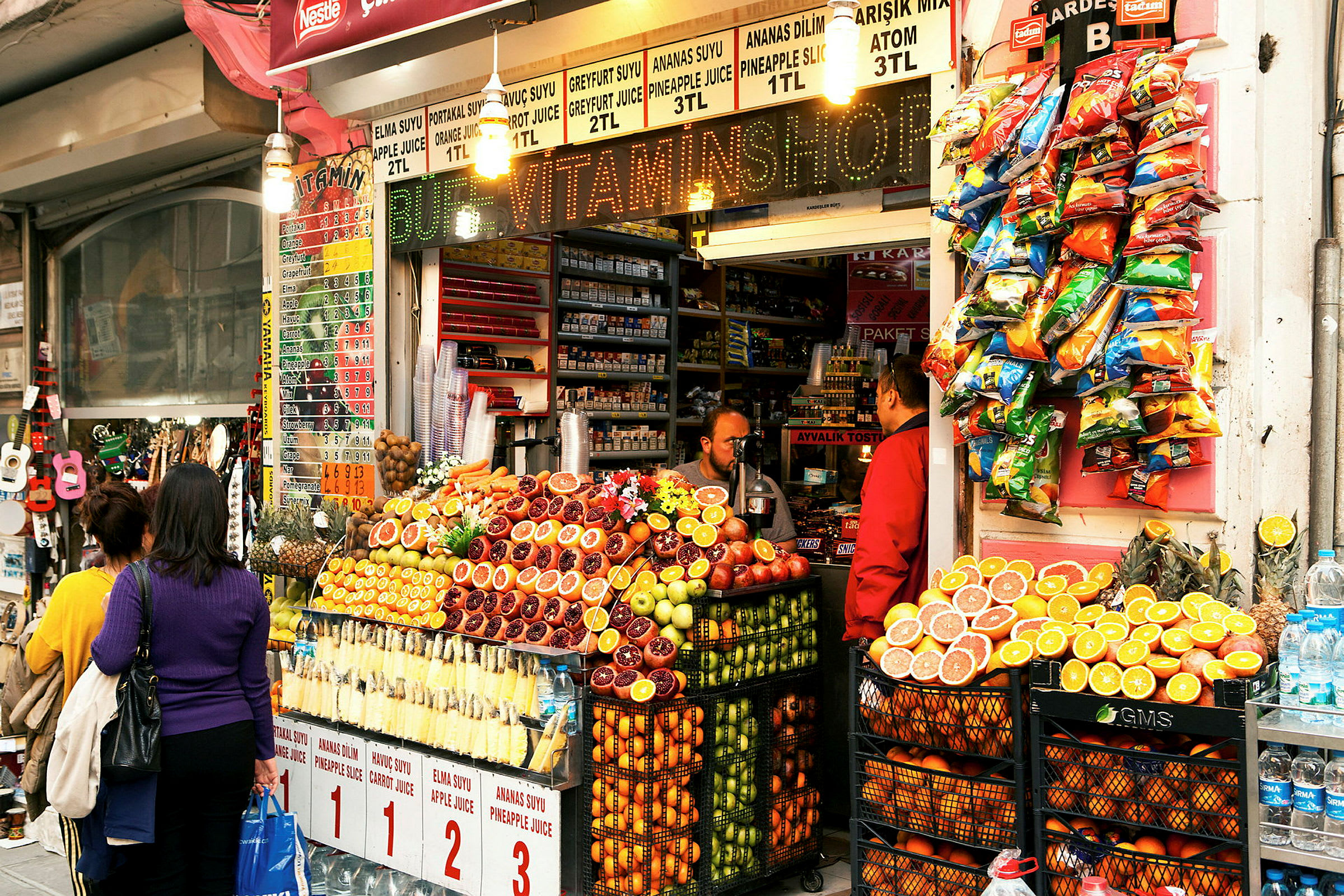 Et frugtstativ foran en butik med friske frugter og juice. (AI-genereret tekst)