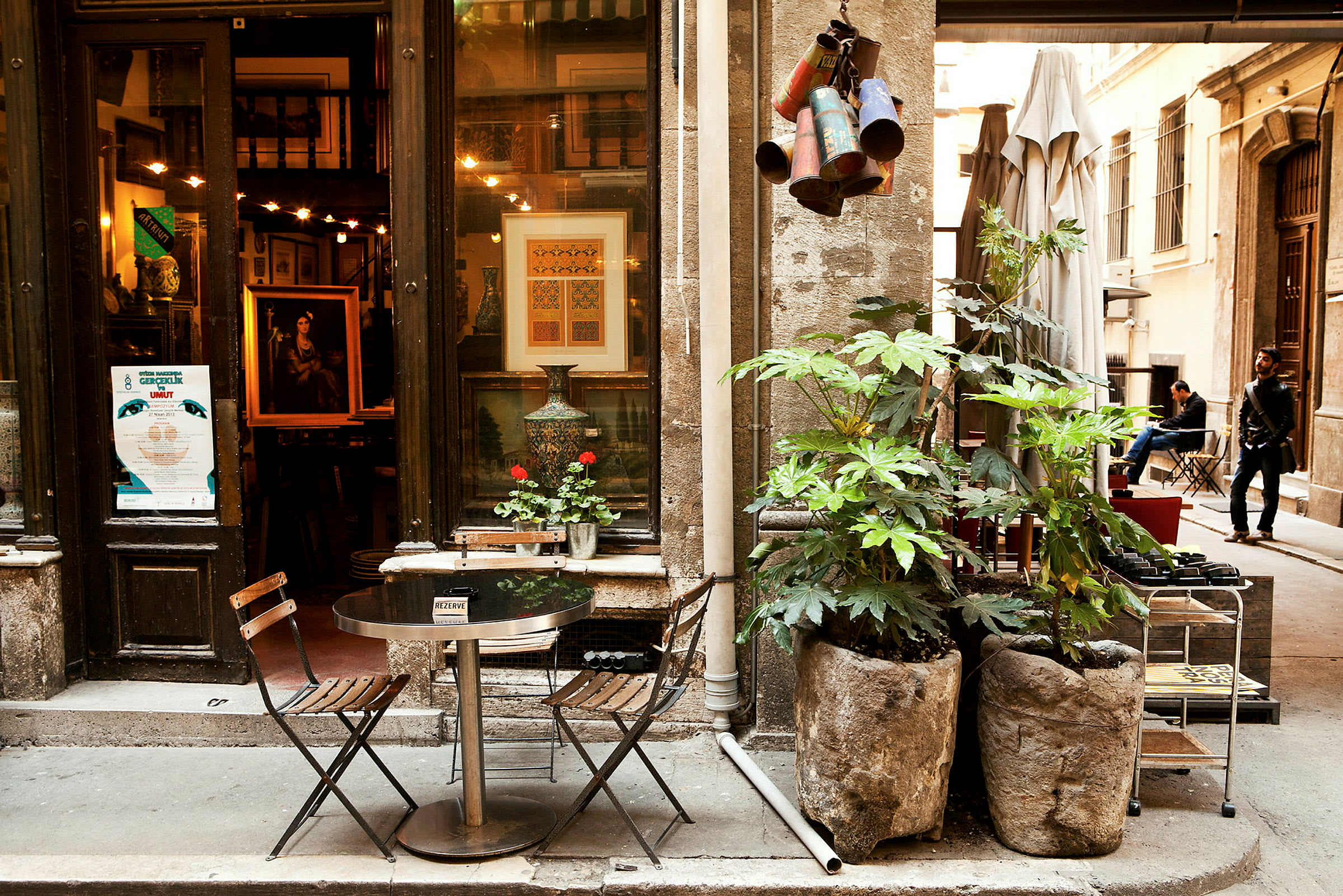 En lille caféplads med to stole og et bord foran en butik med kunstudstilling i et gammelt område. (AI-genereret tekst)