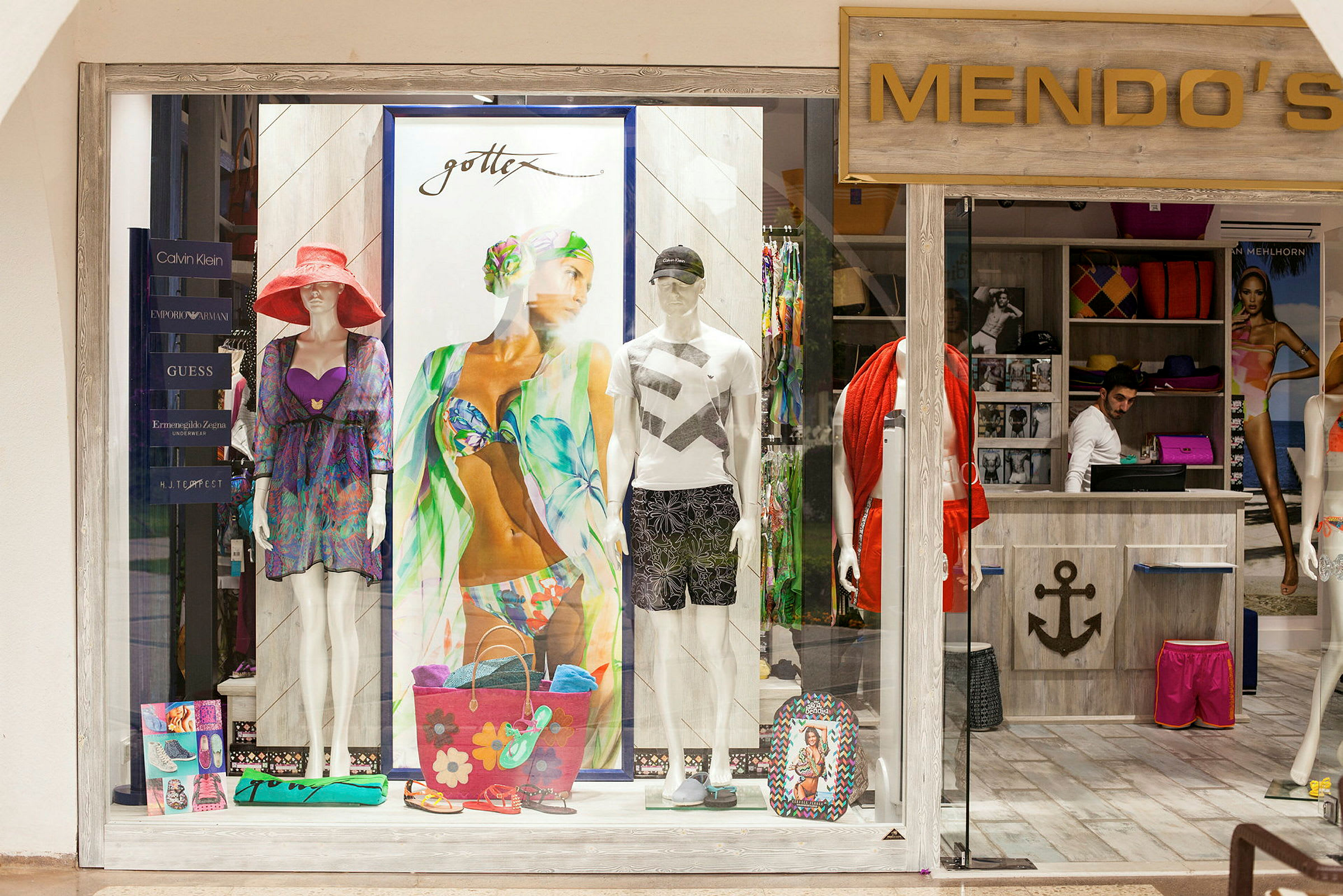Et butiksvindue til en tøjbutik, der viser badetøj og sommeraccessoires. (AI-genereret tekst)