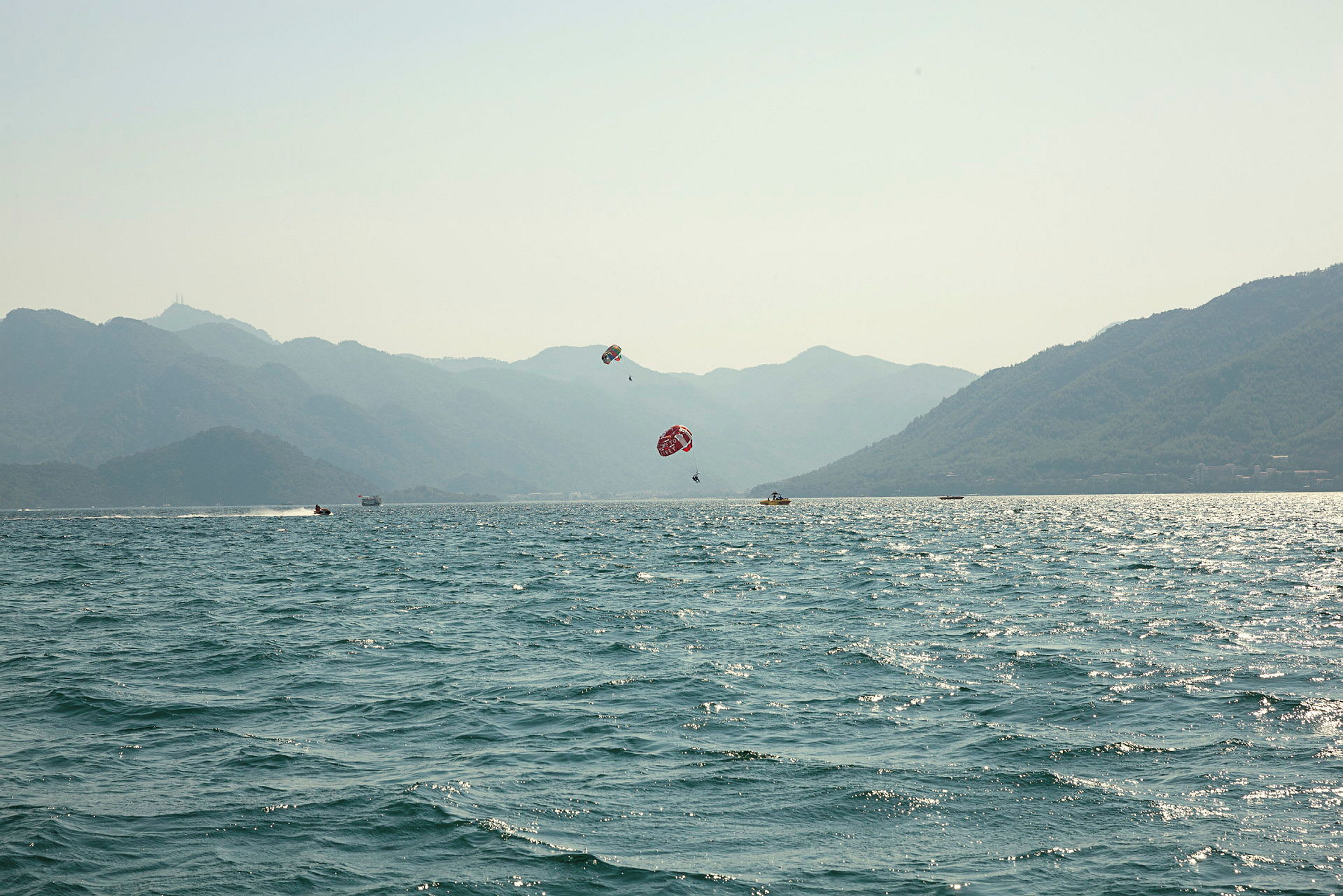 Udsigt over havet med bjerge i baggrunden og personer, der dyrker parasailing. (AI-genereret tekst)