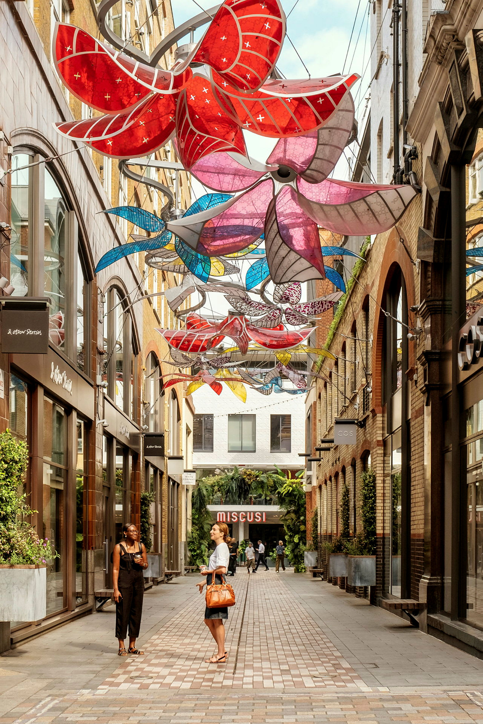 En farverig dekoration i form af blomster hænger over en gade med butikker. (AI-genereret tekst)
