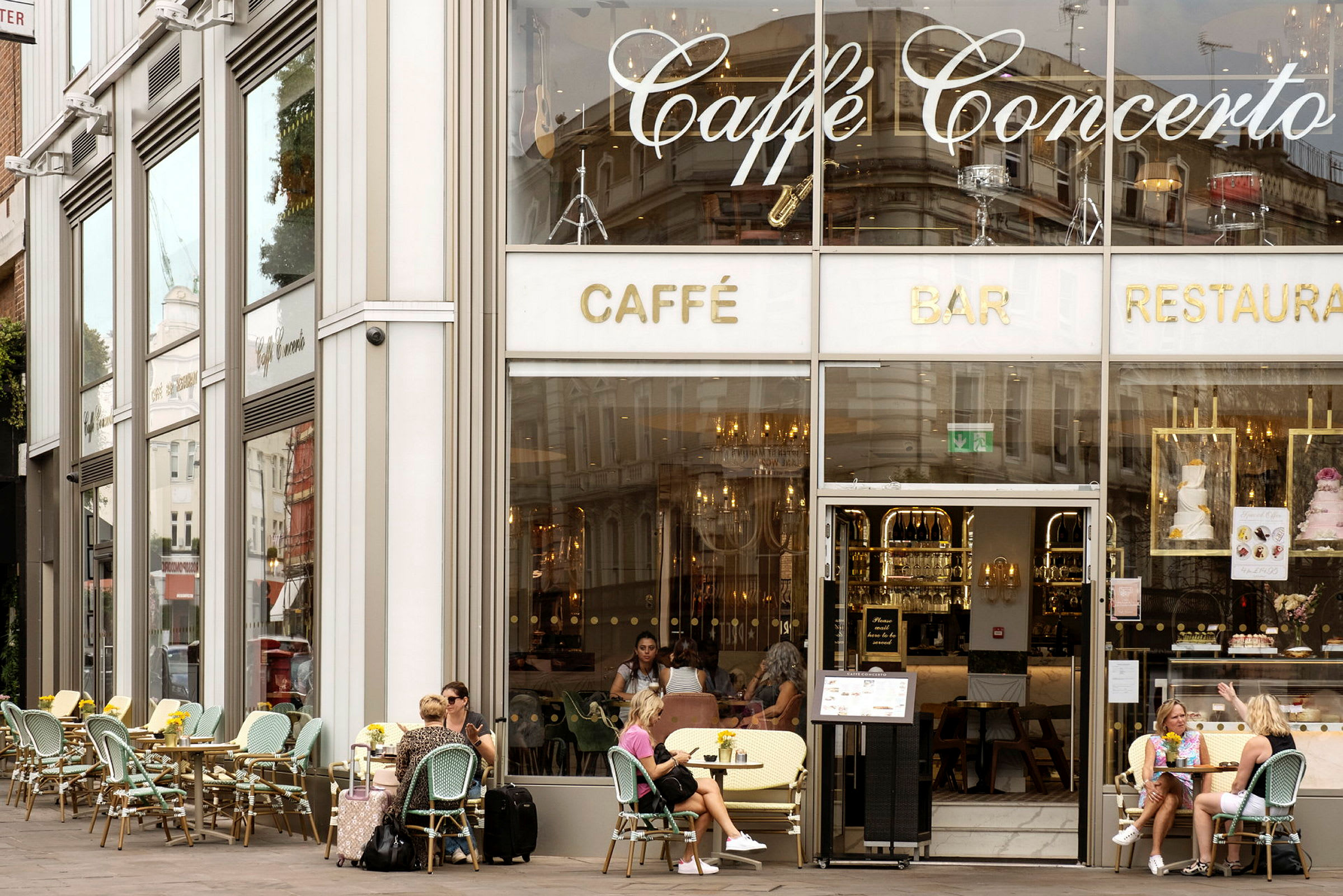 Facaden på en café med store glasvinduer og udendørs servering. (AI-genereret tekst)