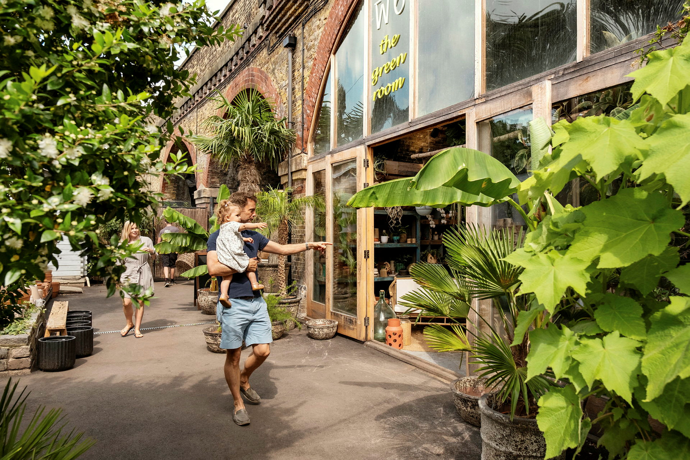 En mand holder et barn foran en butik med planteudsmykning. (AI-genereret tekst)