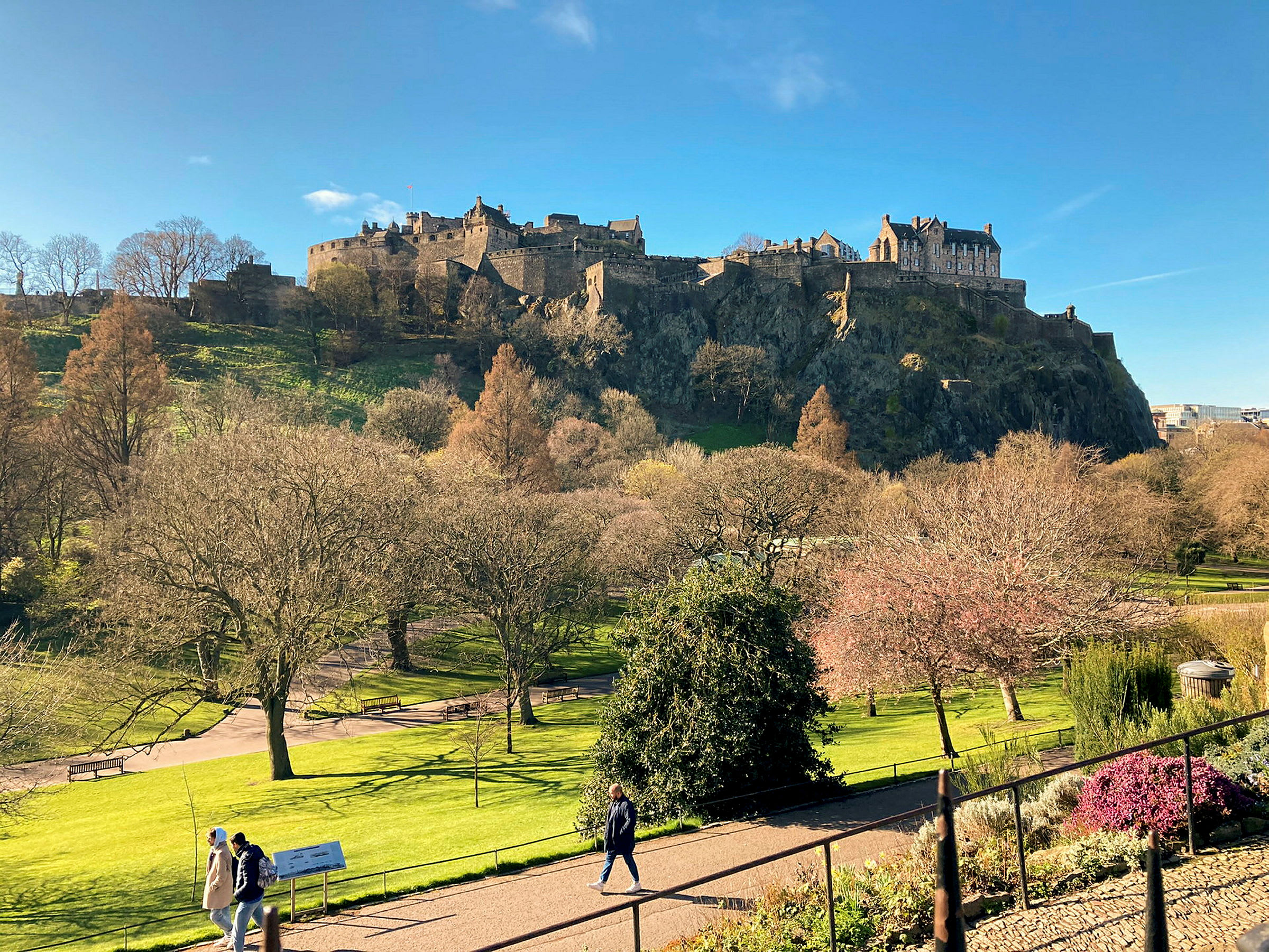 Udsigt over Edinburgh Castle på en solrig dag, omgivet af træer og grønne områder. (AI-genereret tekst)
