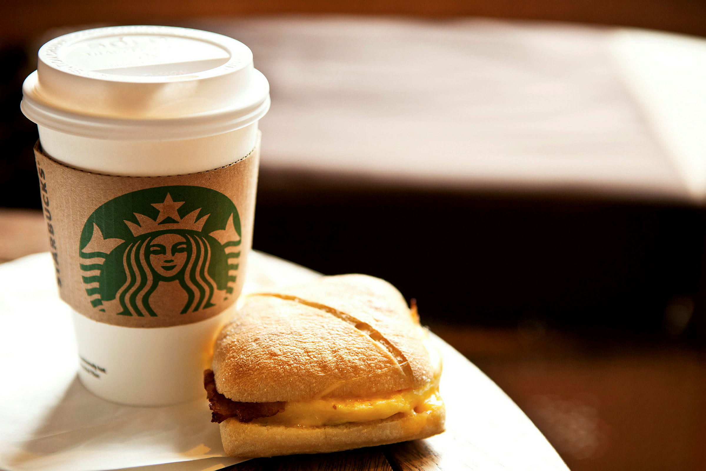 En kop med kaffe og en sandwich på et bord. (AI-genereret tekst)